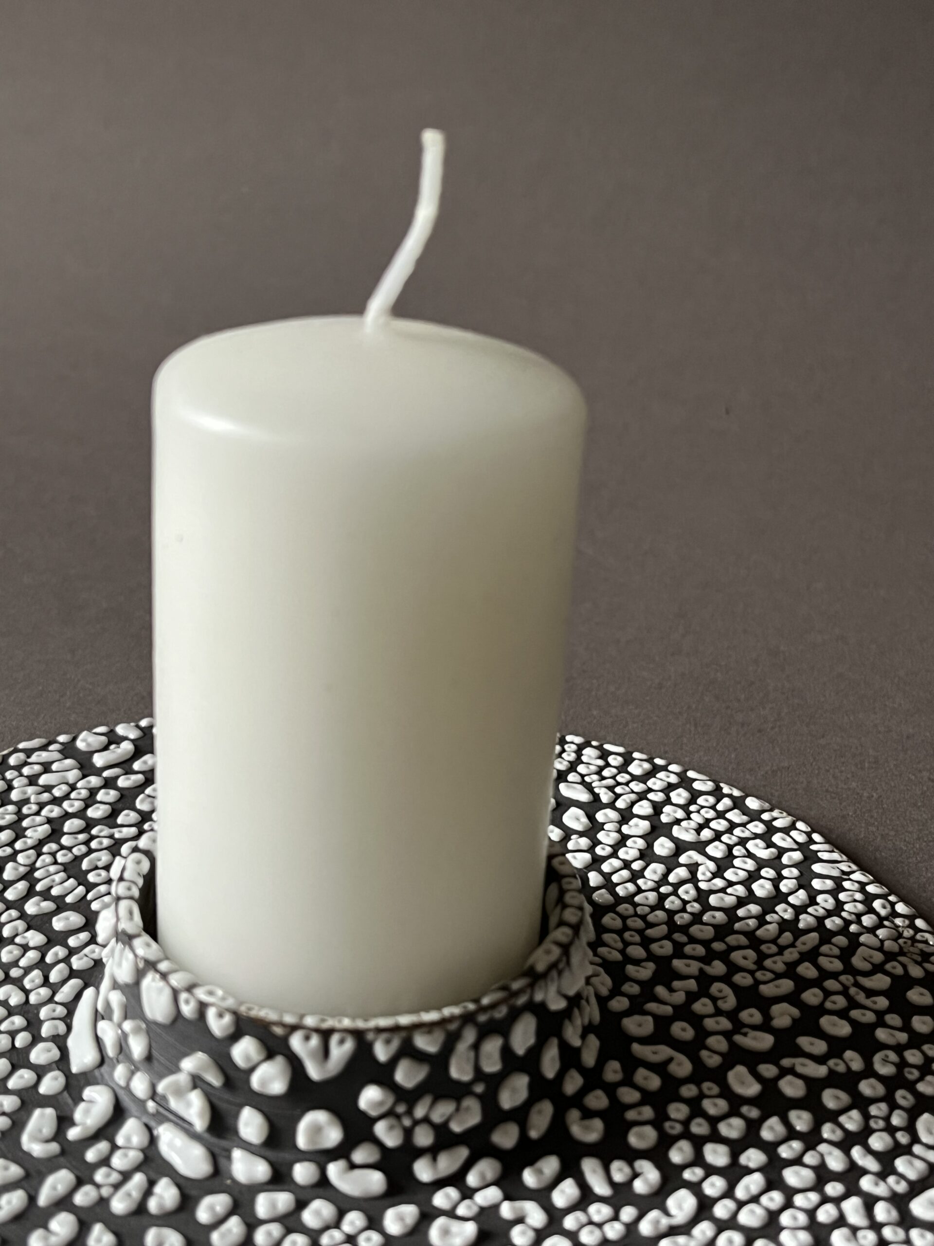 Bougie blanche cylindrique posée dans le bougeoir plat Winter, émail rétracté blanc en billes