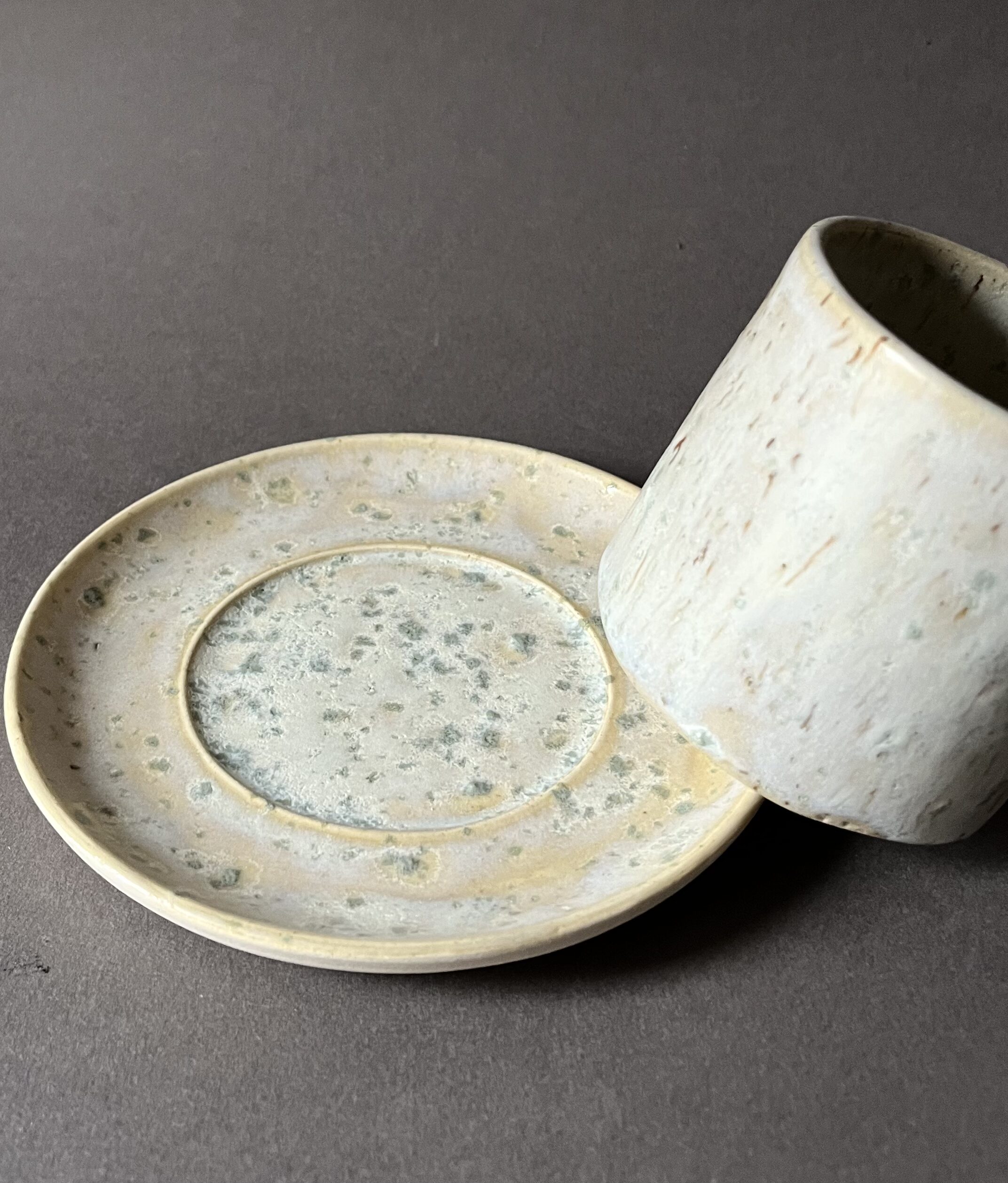 Tasse Steph en grès à l'émail satiné beige et vert appuyée sur le bord de sa soucoupe assortie
