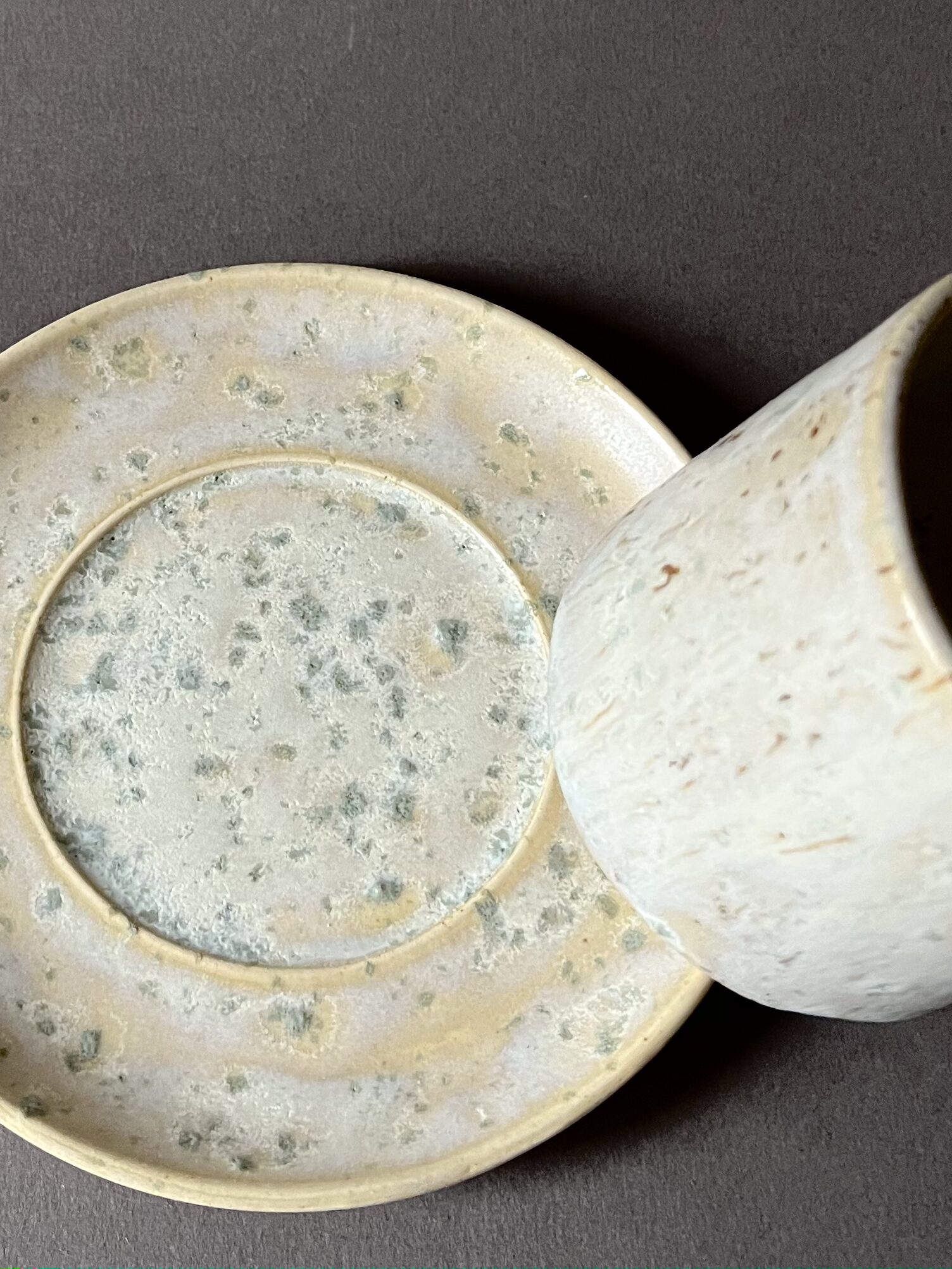 Gros plan sur la soucoupe Steph à l'émail satiné tacheté de vert, tasse posée sur le bord