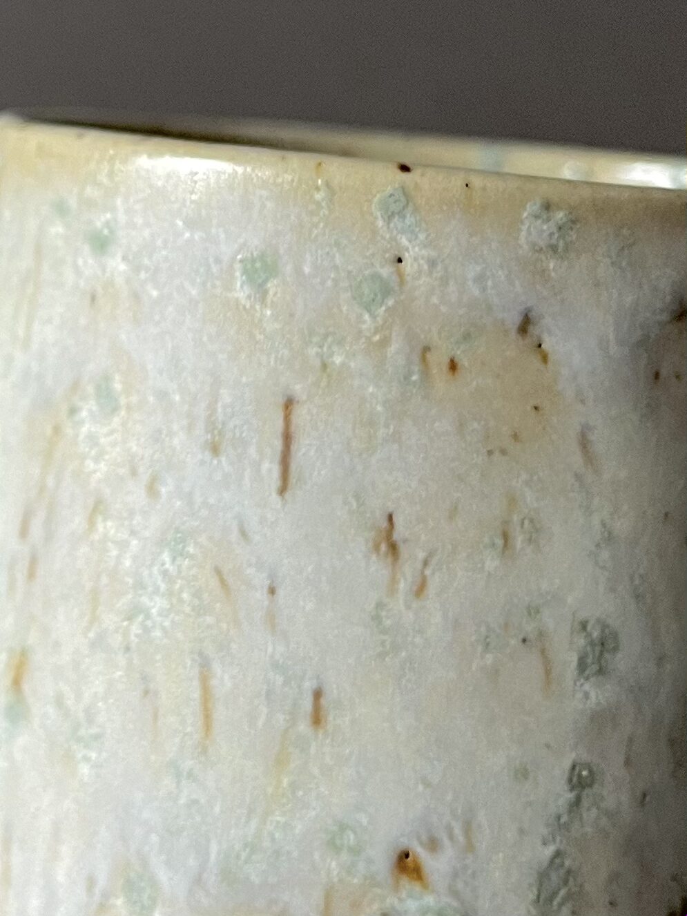 Gros plan sur la paroi de la tasse Steph, émail satiné blanc, beige et vert avec taches brillantes