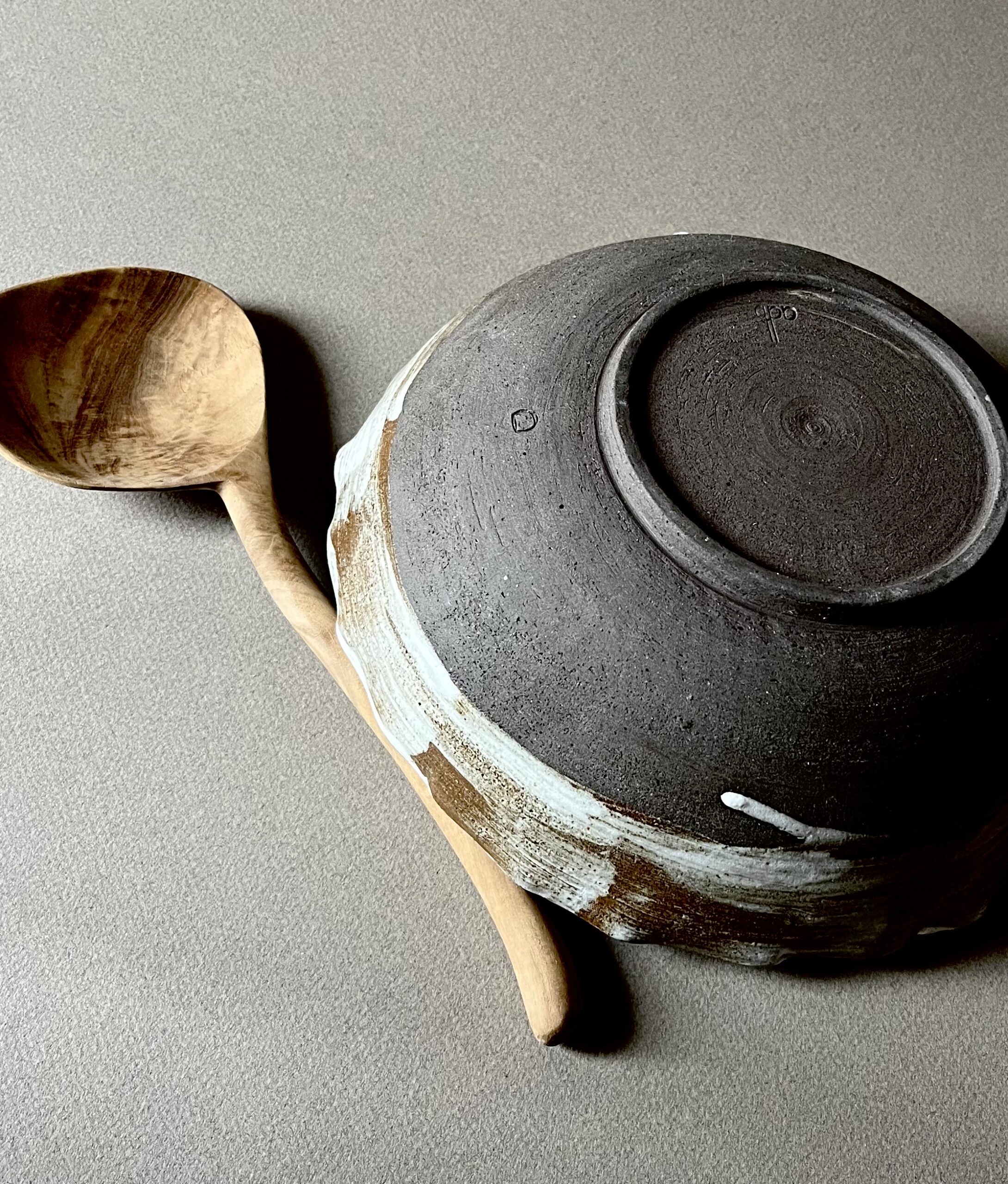 Saladier marbré retourné montrant son pied en grès sombre brut, cuillère en bois à côté