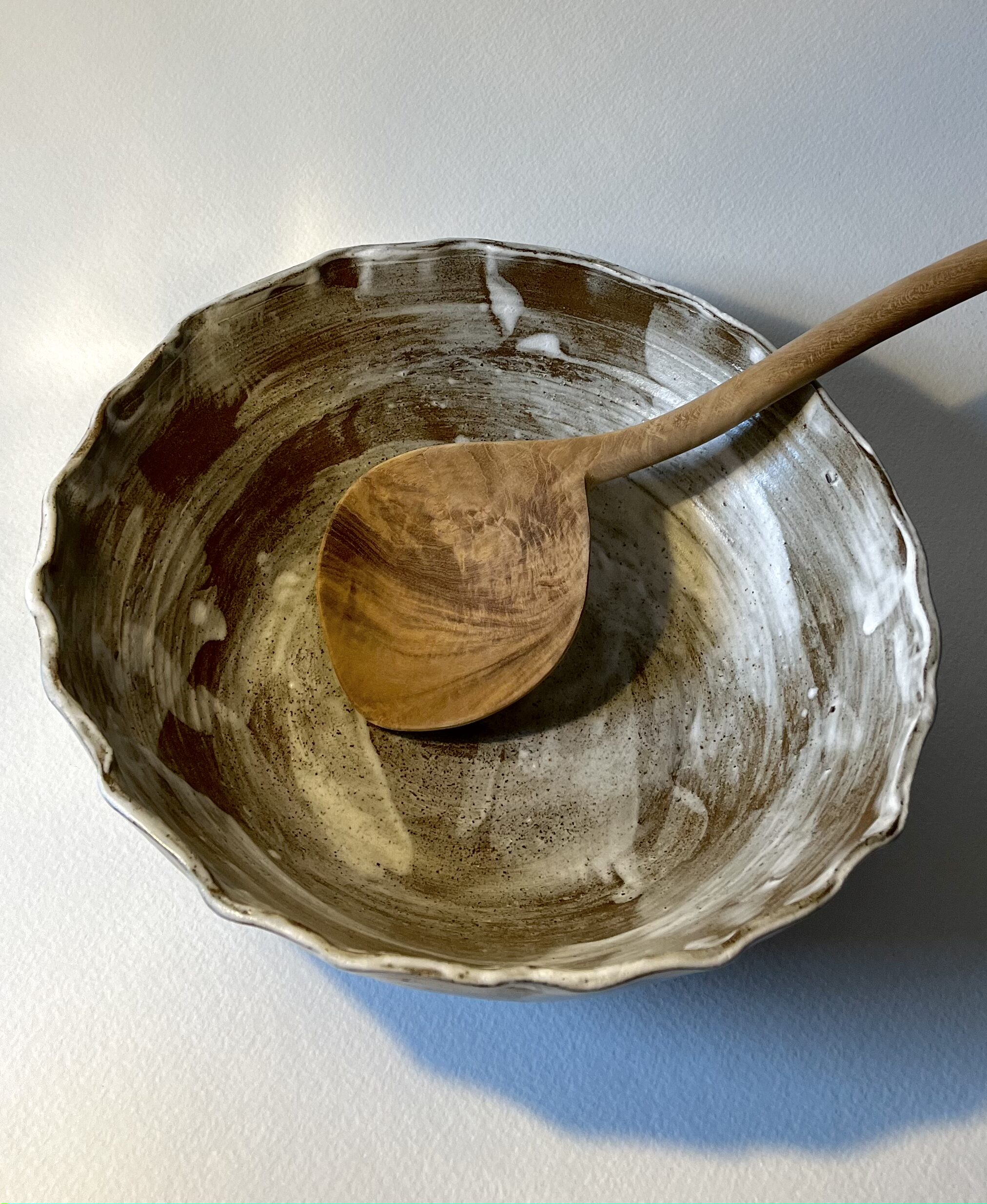 Saladier marbré marron et blanc vu de dessus avec une grande cuillère en bois posée dedans
