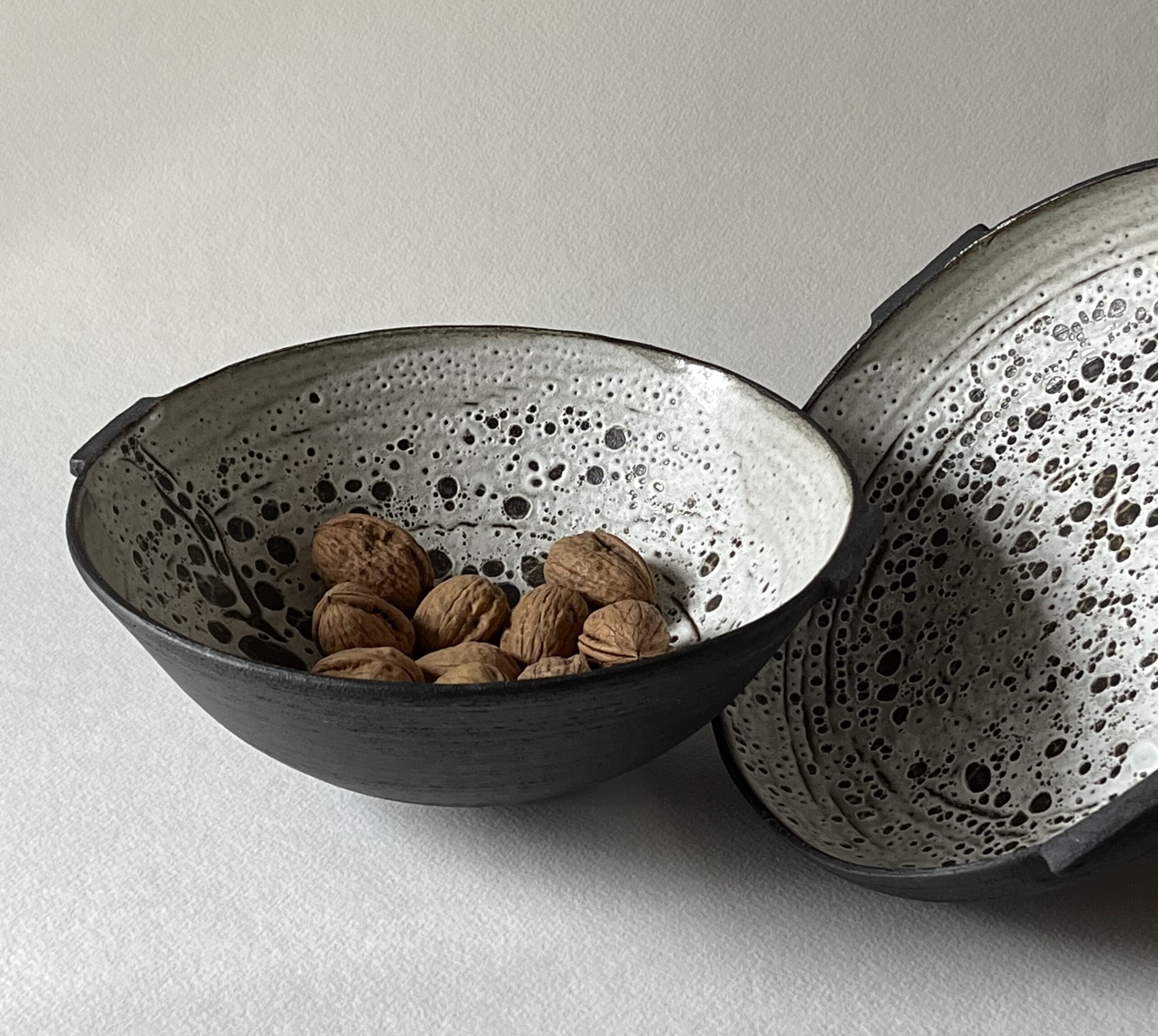 Deux coupes Rocaille en grès noir chamotté, intérieur émail blanc à pastilles, garnies de noix