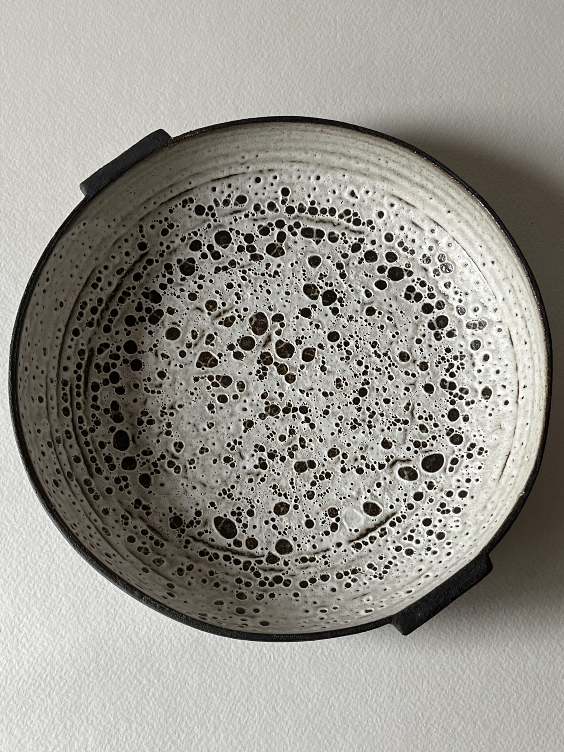 Coupe Rocaille plate vue de dessus, émail blanc velours à pastilles découvertes sur grès noir, deux petites anses