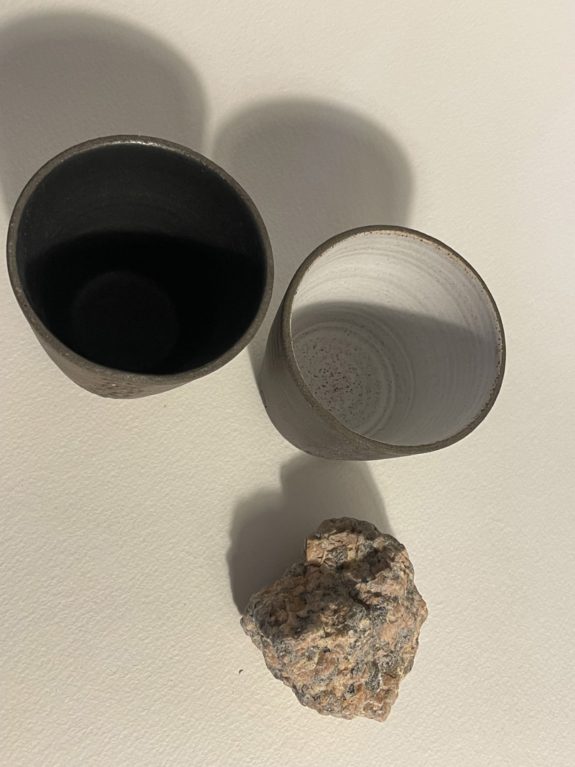 Deux gobelets Treb vus de dessus, intérieurs émaillés noir mat et blanc mat, granit rose à côté