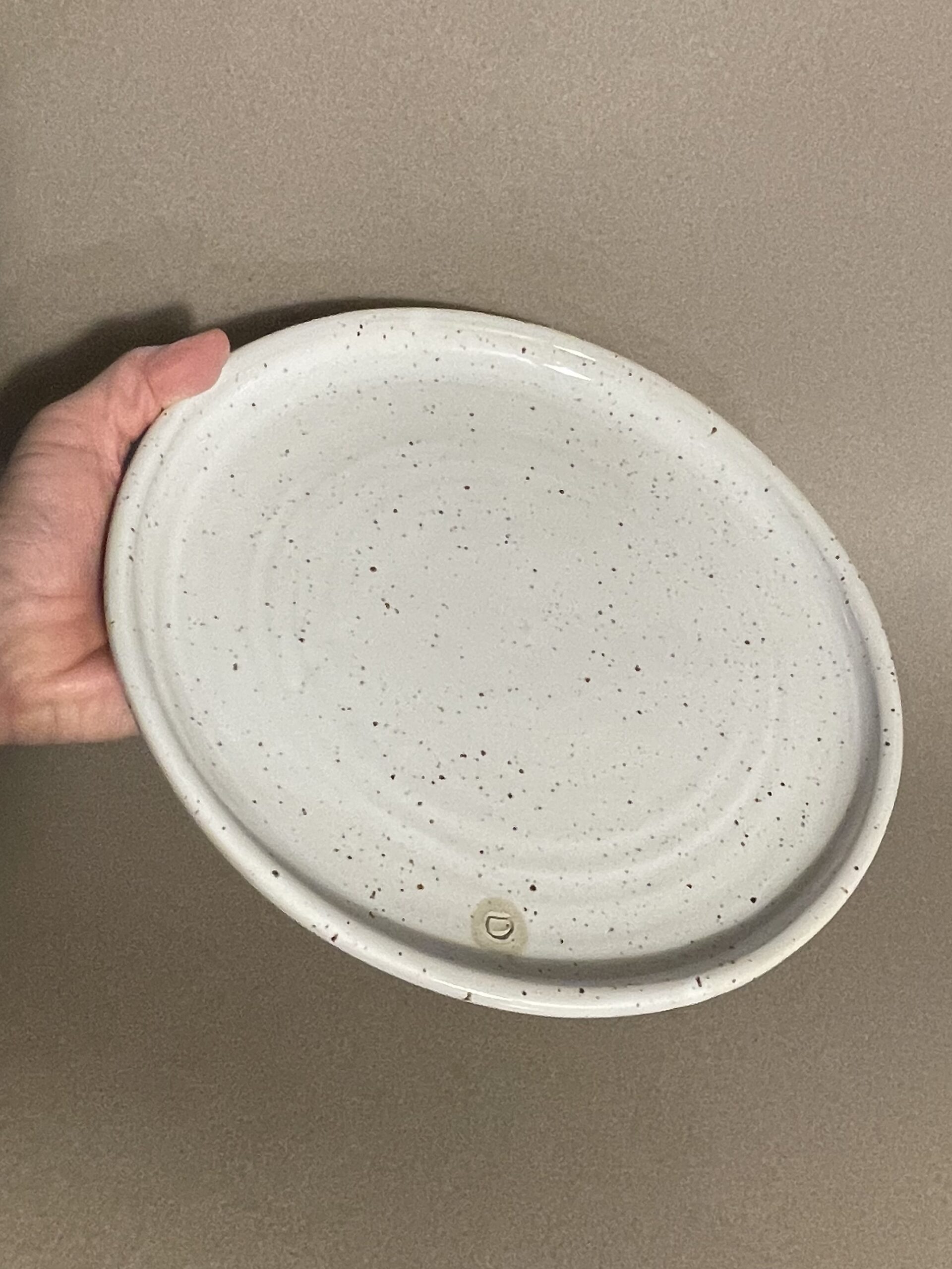Assiette plate Maya en grès pyrité émaillé blanc brillant tenue en main, logo adb en creux