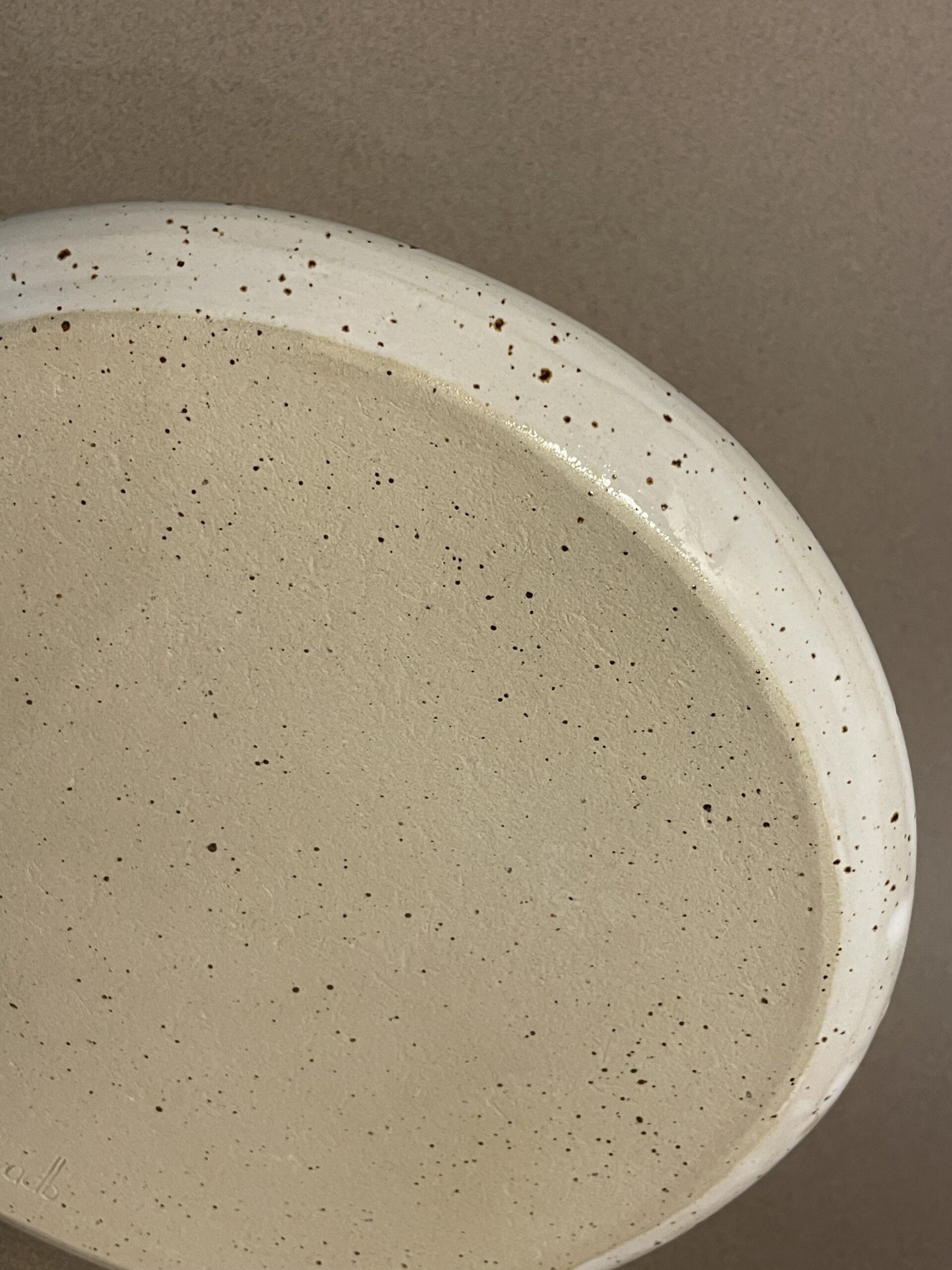 Dessous de l'assiette plate Maya, grès pyrité laissé brut et rebord émaillé blanc