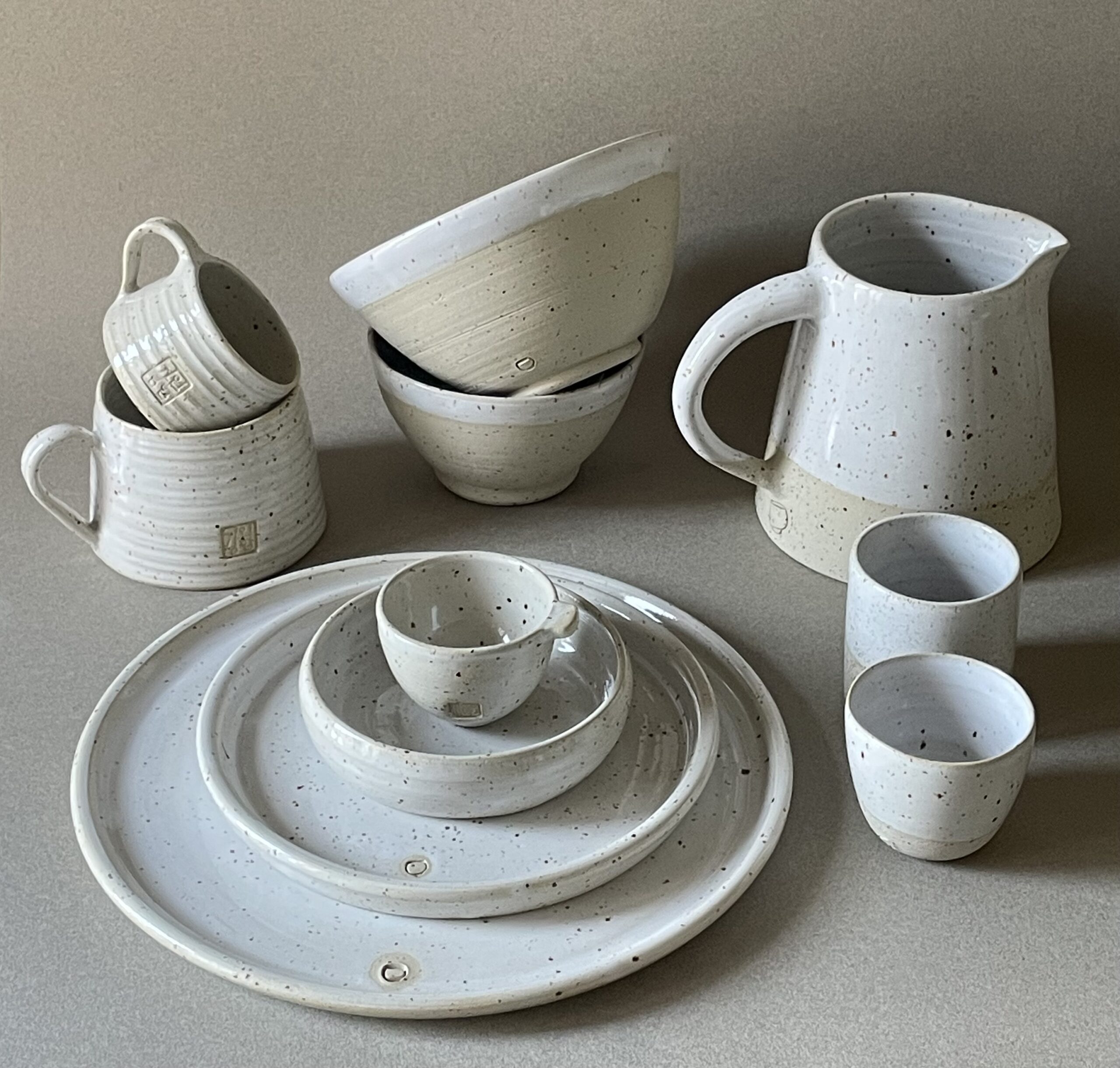 Ensemble de la collection Maya vu de trois quarts : assiettes empilées, bols, tasses, gobelets et pichet