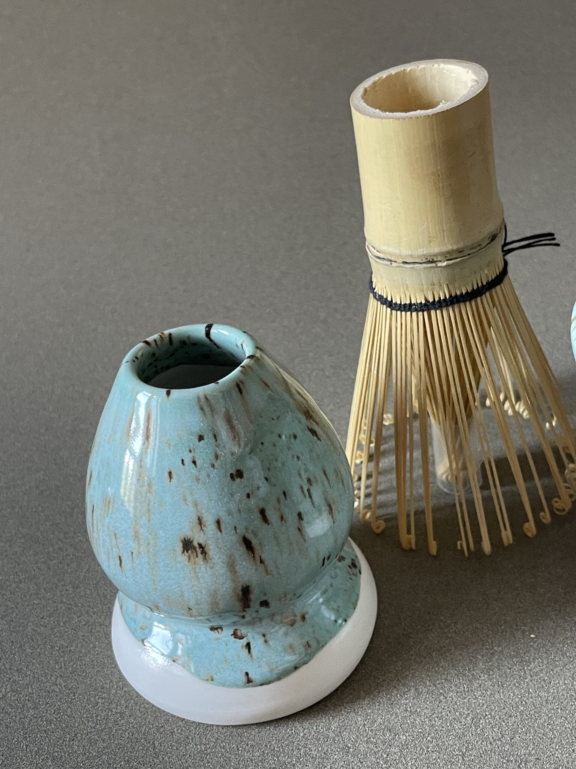 Repose-fouet à matcha Osaka en porcelaine céladon tacheté, avec fouet en bambou posé à côté
