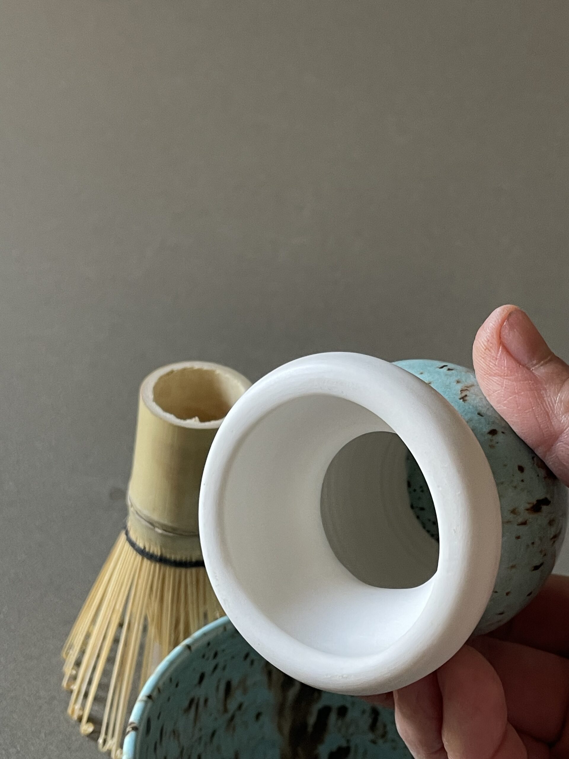 Repose-fouet à matcha Osaka en porcelaine tenu en main, intérieur blanc et extérieur céladon, fouet en bambou