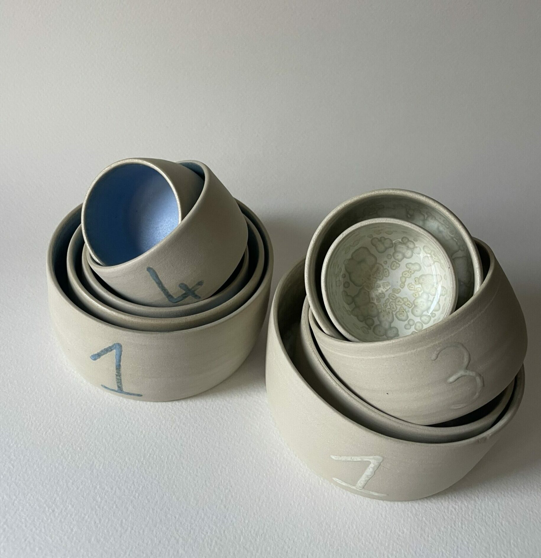 Deux jeux de bols gigognes numérotés en grès brut, l'un émaillé bleu et l'autre blanc nacré à l'intérieur