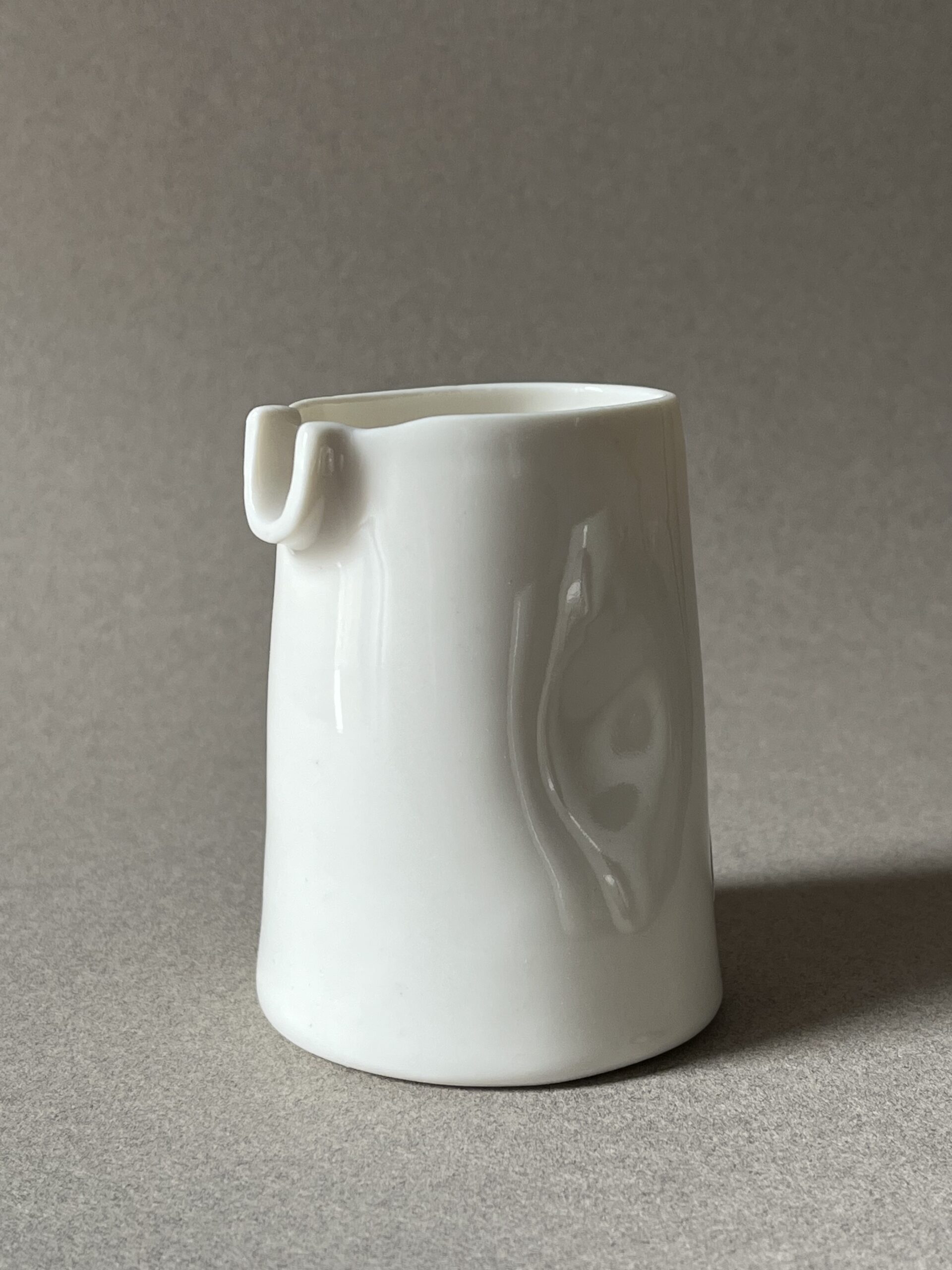 Petite saucière verseuse en porcelaine blanche brillante à renfoncements, vue de face sur fond gris