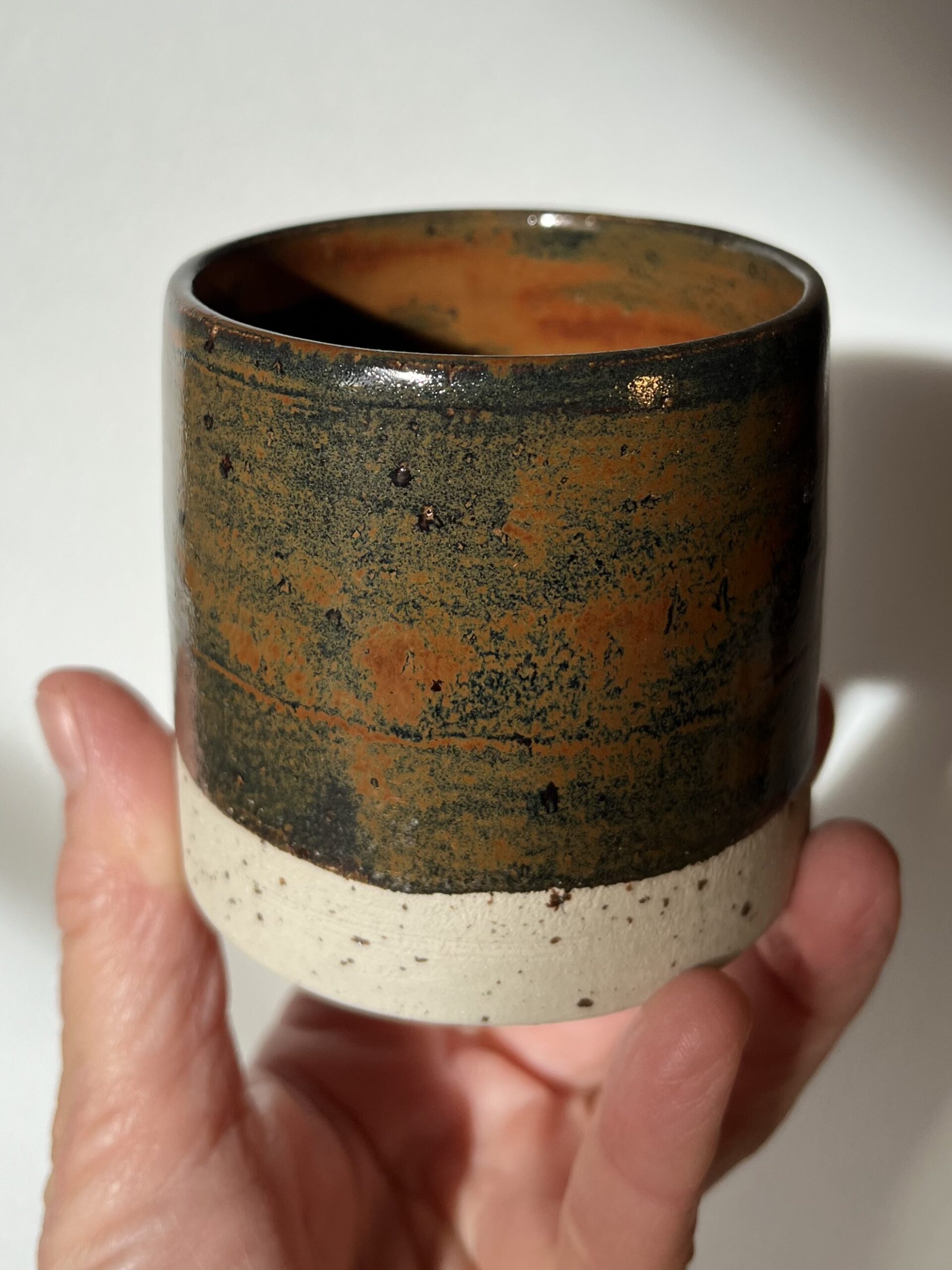Gobelet Steph en grès à l'émail automne brillant, orange et vert sombre, tenu en main, base brute