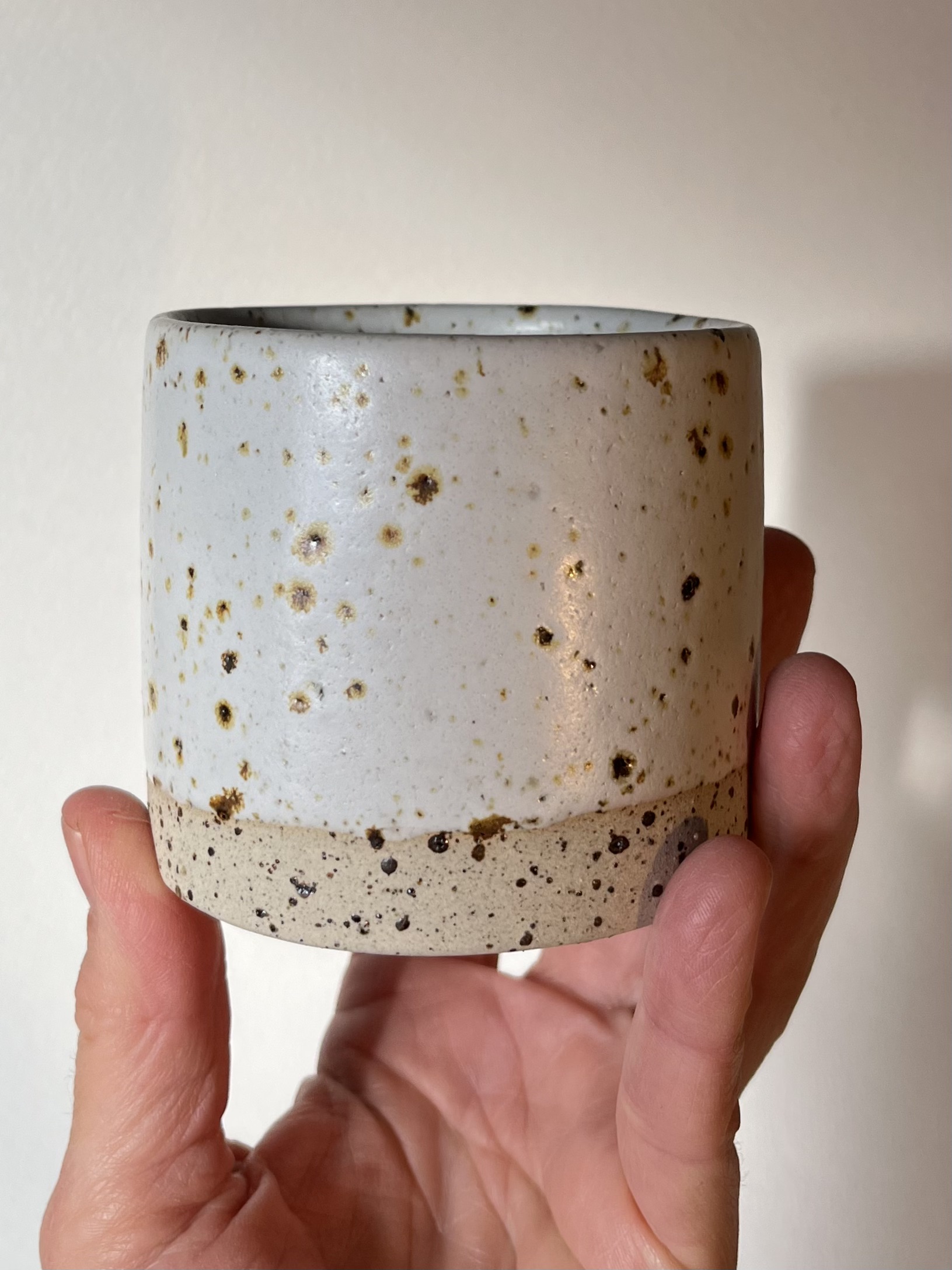 Gobelet Steph en grès pyrité à l'émail blanc brillant moucheté, tenu en main, base brute