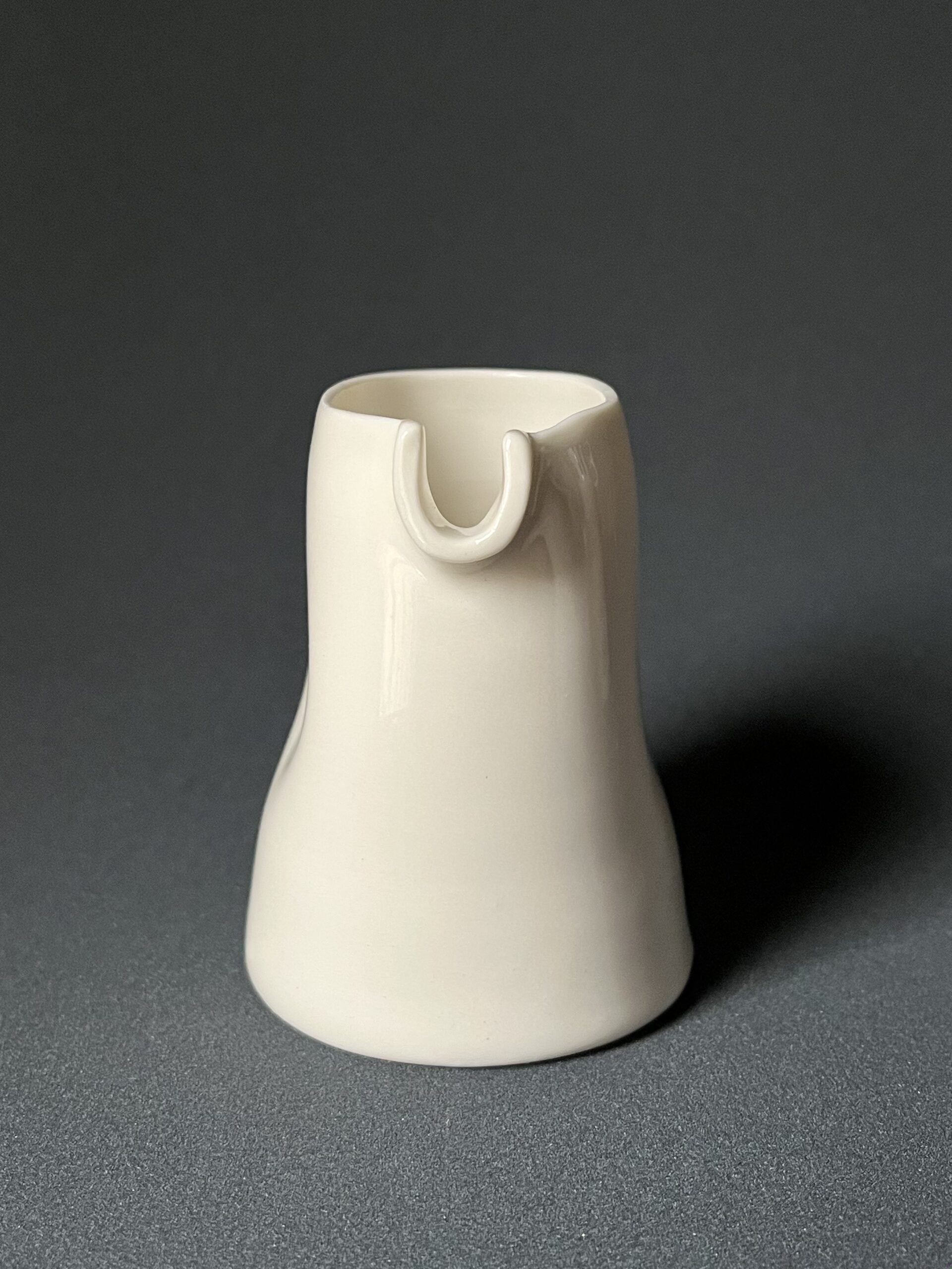 Saucière verseuse en porcelaine blanche vue de face, bec verseur en U et parois pincées, fond sombre