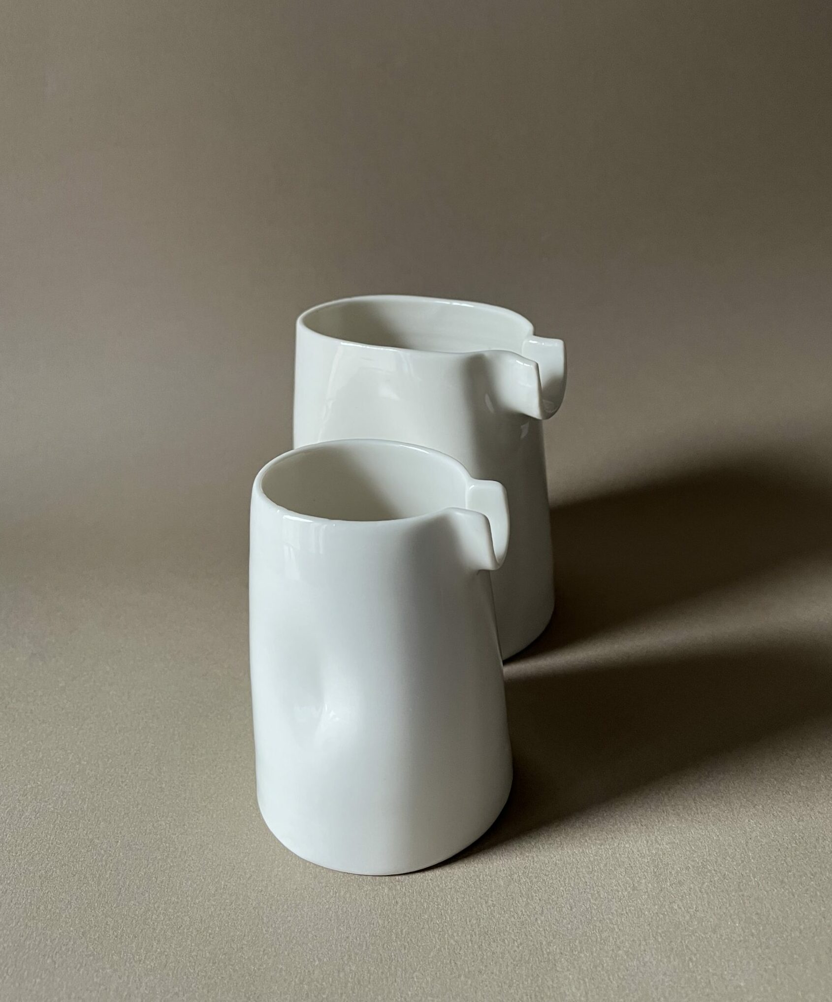 Deux saucières verseuses en porcelaine blanche de tailles différentes, becs en U, sur fond beige