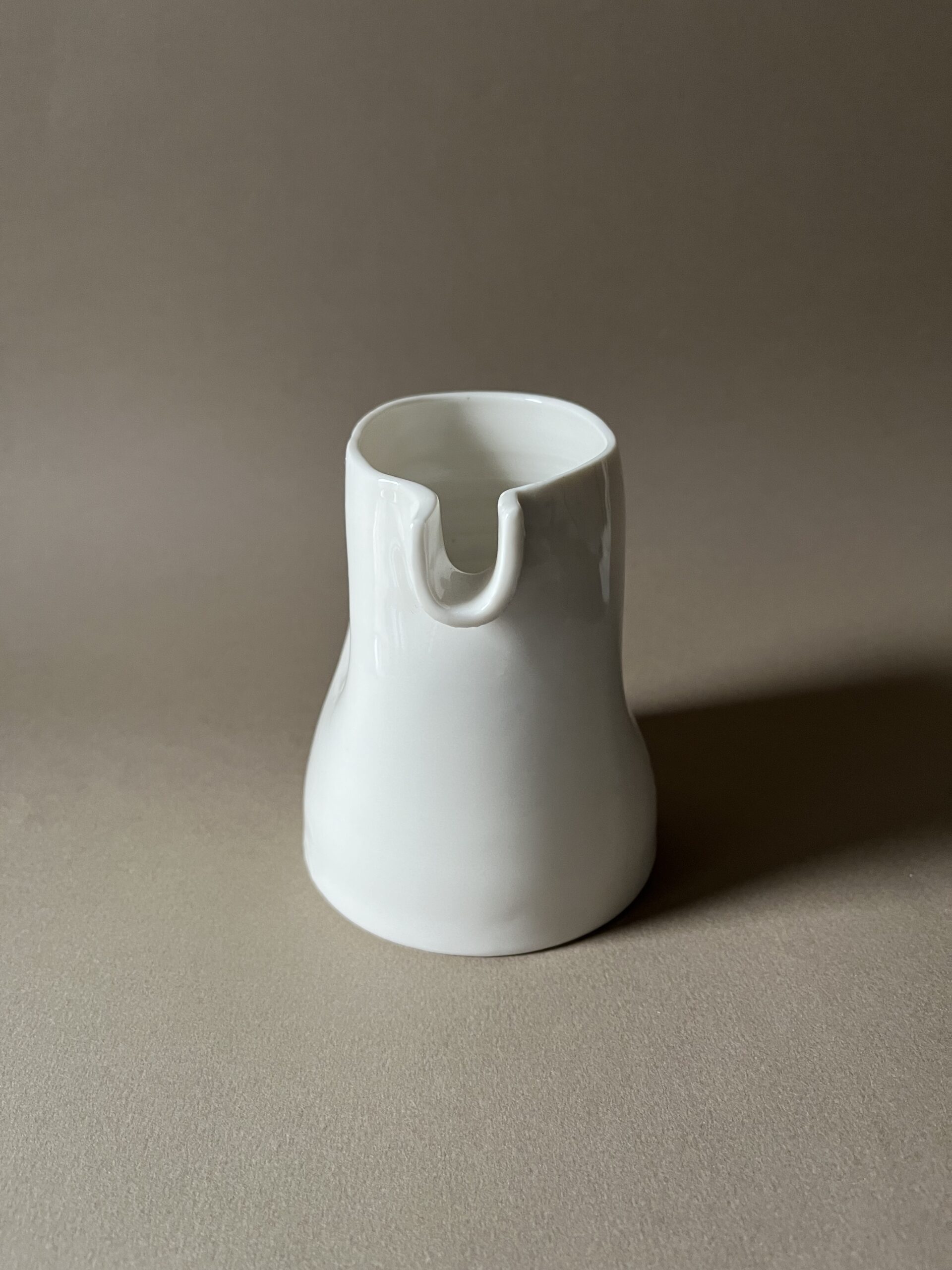 Petite saucière verseuse en porcelaine blanche vue de face, bec en U, sur fond beige