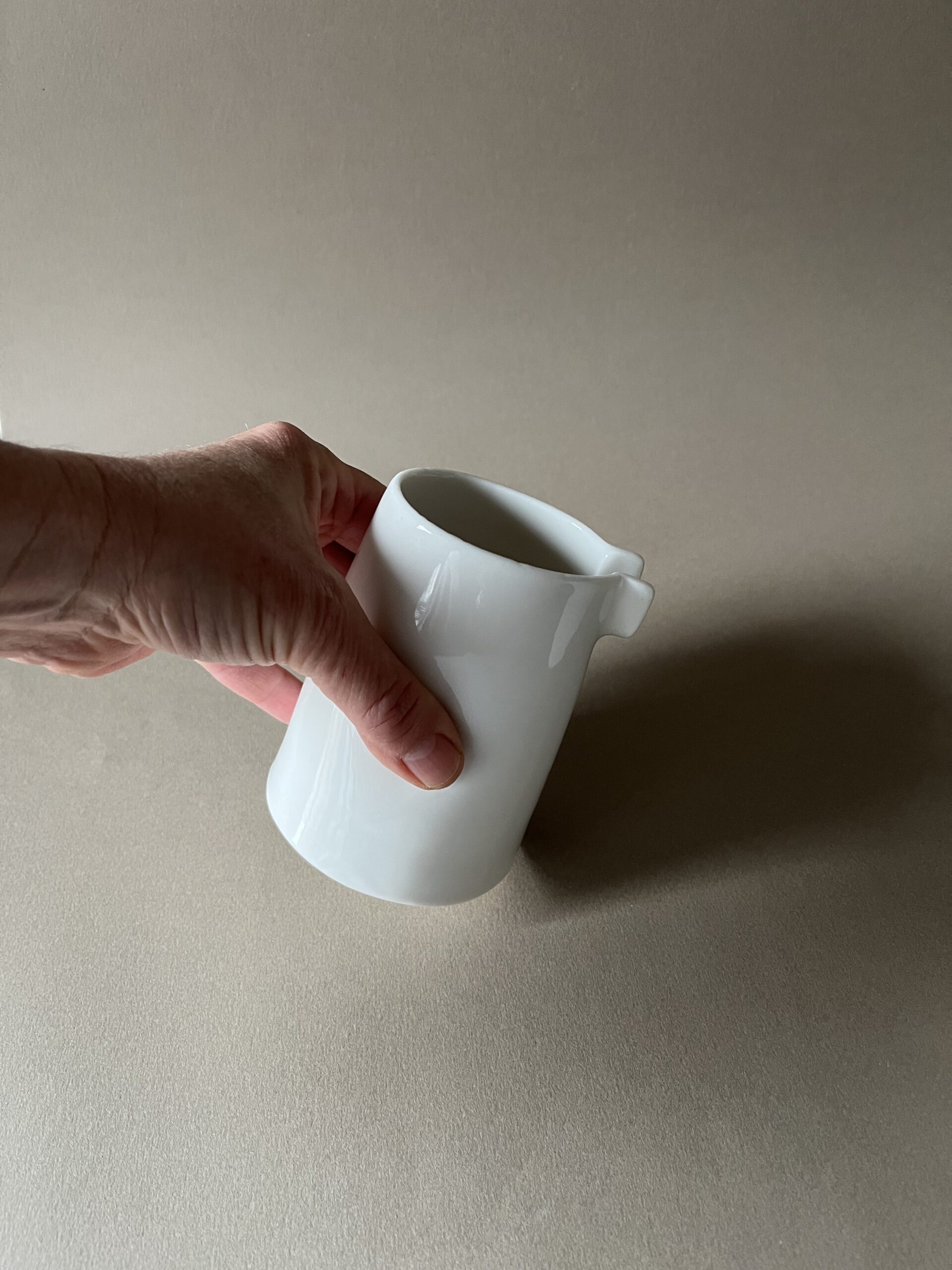 Petite saucière verseuse en porcelaine blanche tenue en main par son renfoncement