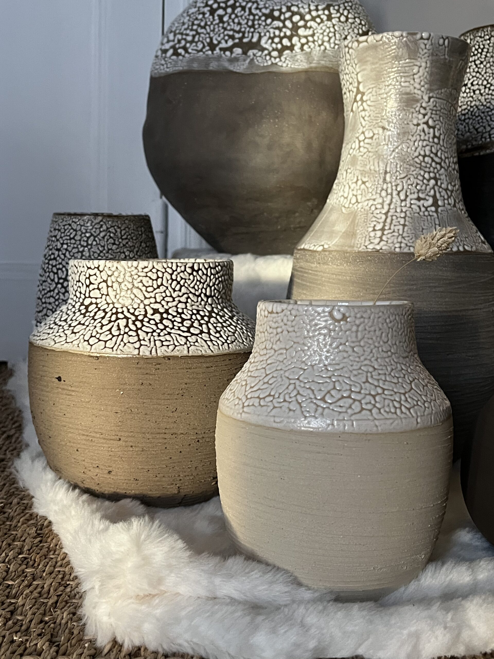 Vases Winter en grès beige et brun aux cols émaillés blanc rétracté, posés sur une peau blanche, vue rapprochée