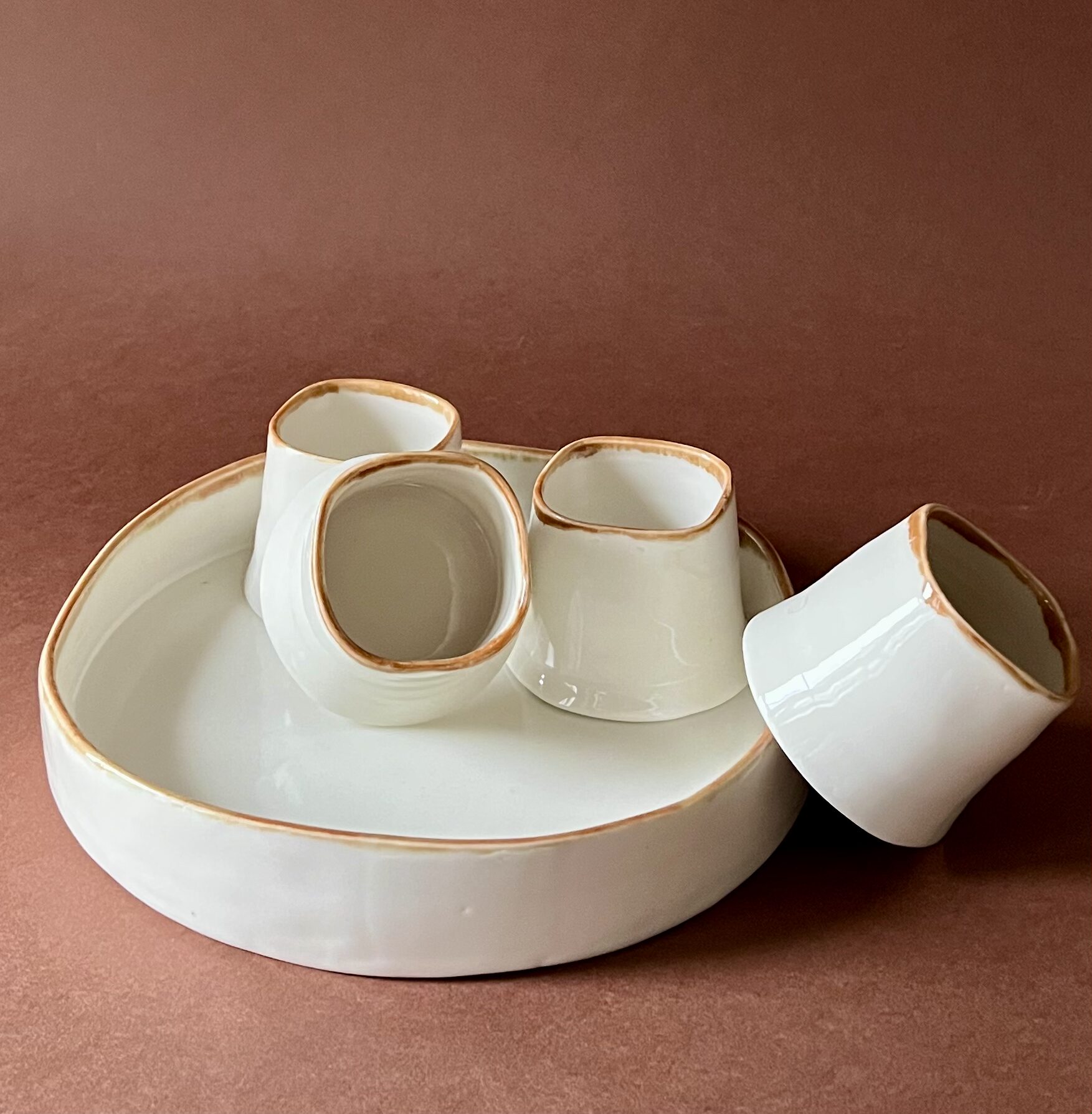 Set à café Ulysse en porcelaine blanche à liseré marron, tasses carrées sur plateau rond, l'une couchée