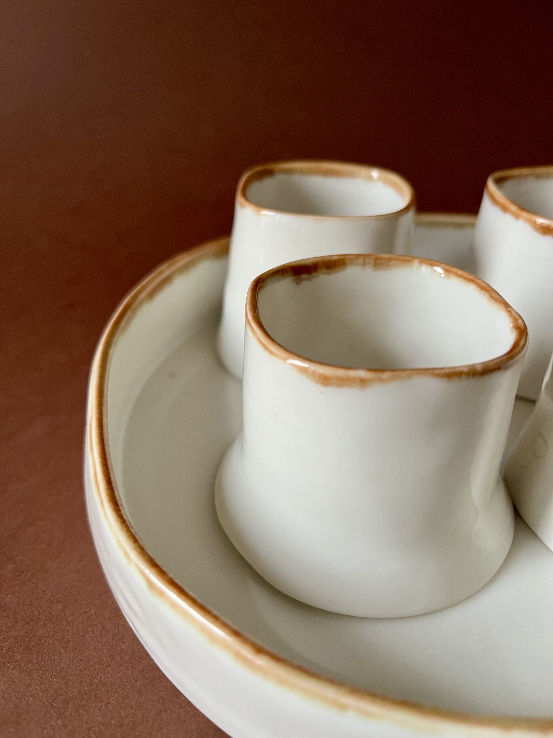 Gros plan sur les lèvres à liseré marron des tasses Ulysse en porcelaine blanche sur leur plateau