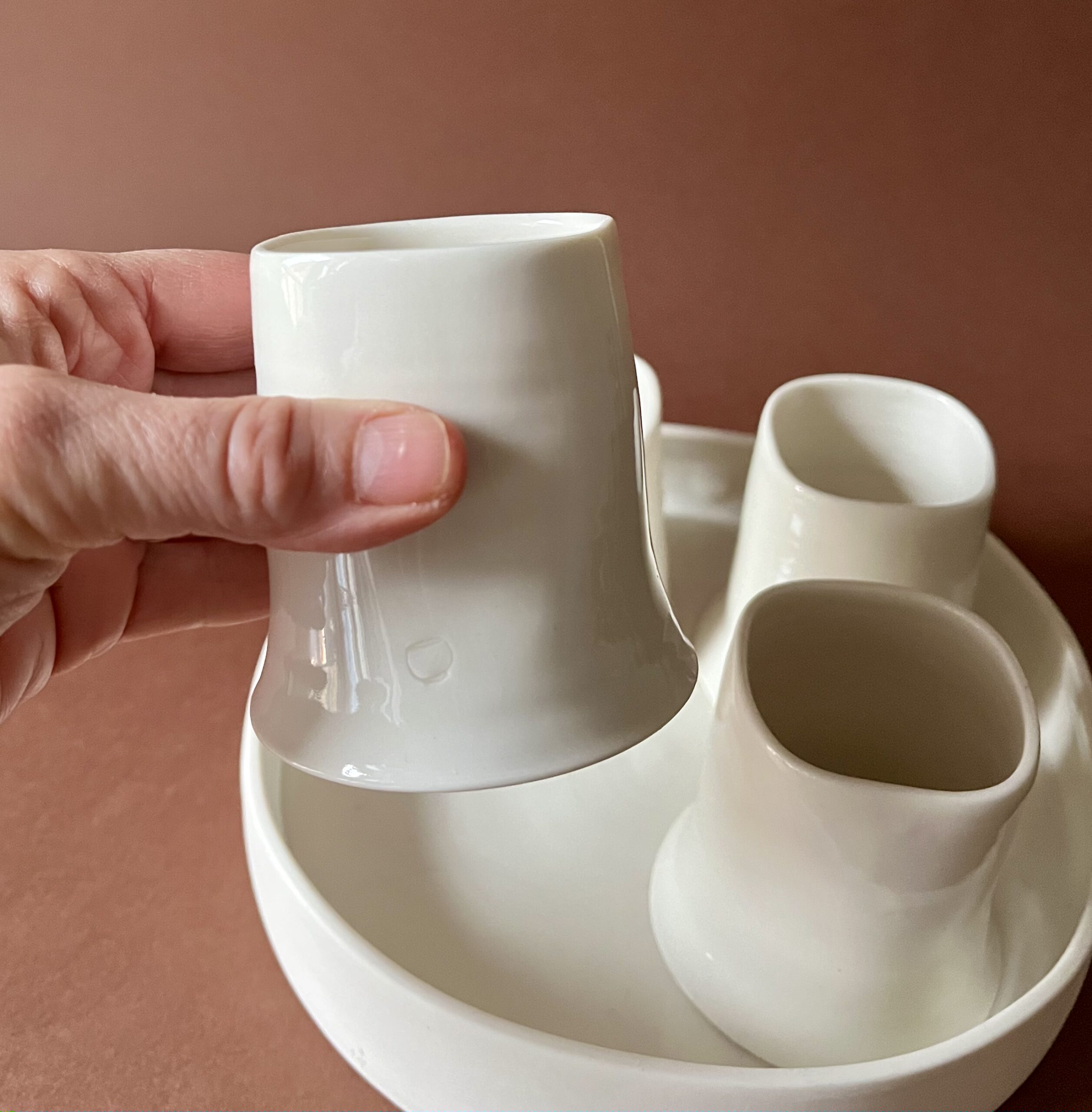 Tasse Ulysse blanche tenue en main au-dessus du set, tasses et plateau en porcelaine blanche