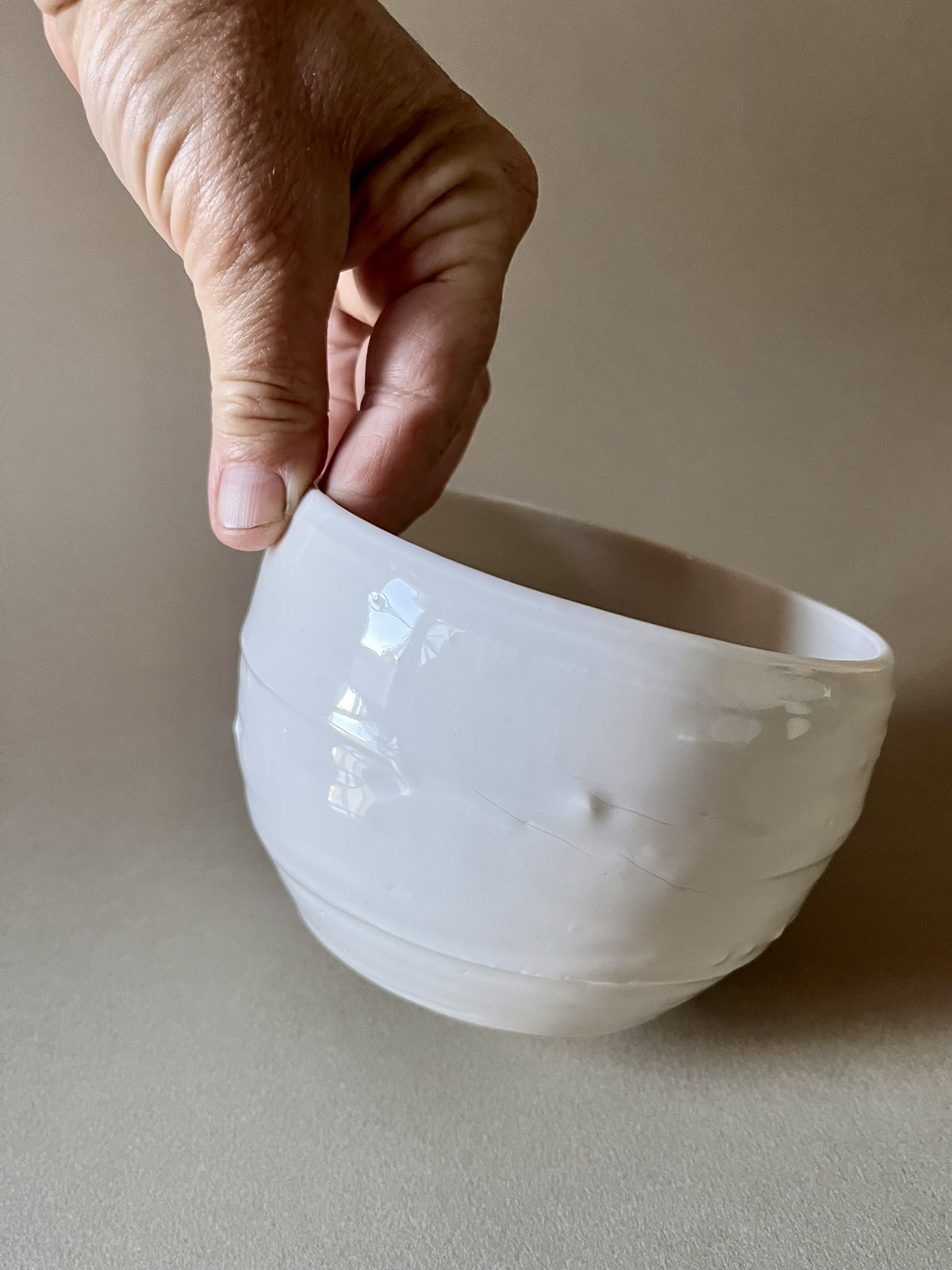Bol Purete en porcelaine blanche tenu par le bord entre deux doigts, émail brillant