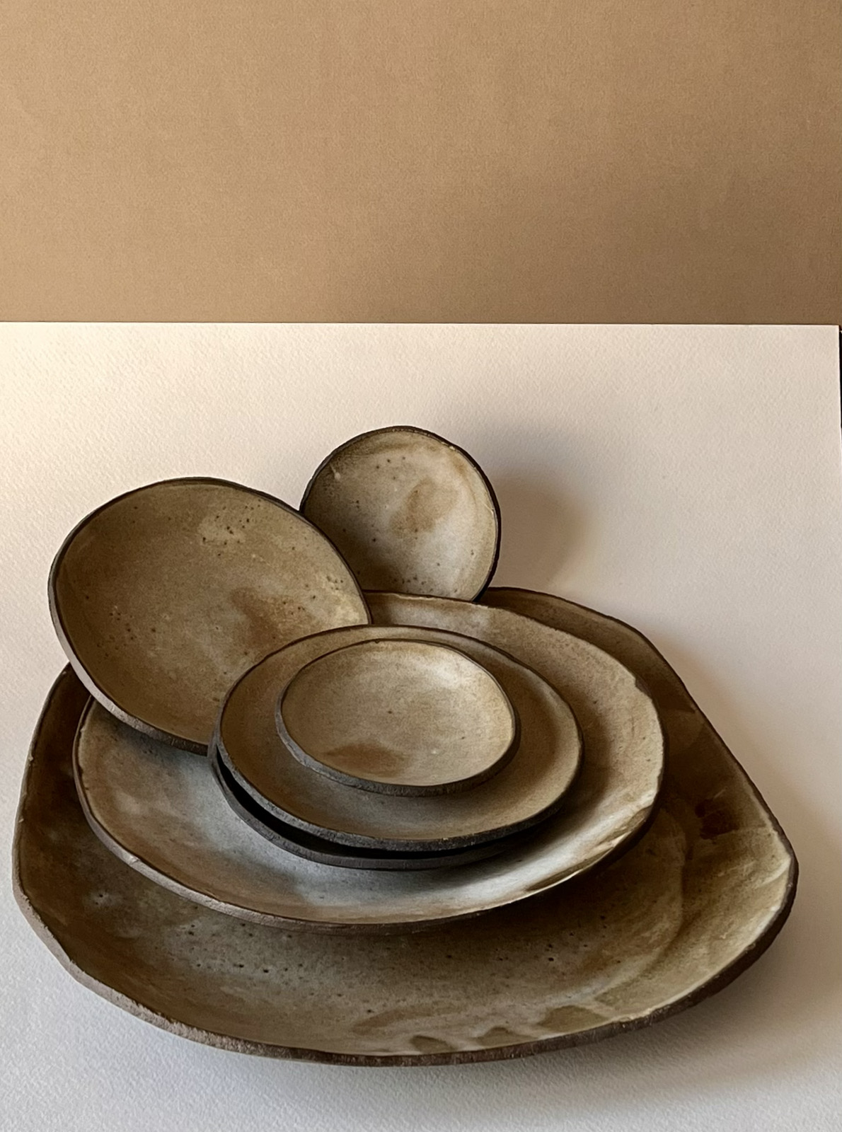 Pile d'assiettes et coupelles en grès brun foncé à l'émail beige nuageux, formes libres