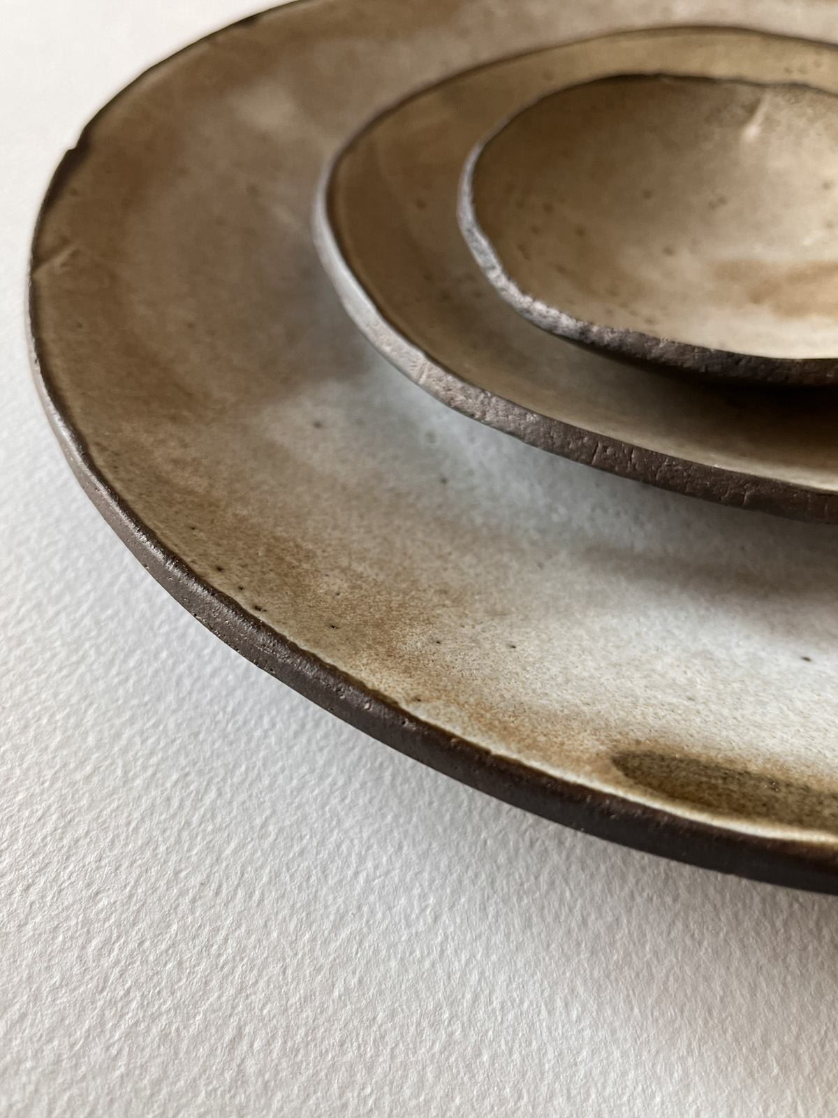 Gros plan sur les bords irréguliers d'assiettes en grès brun à l'émail beige nuageux empilées