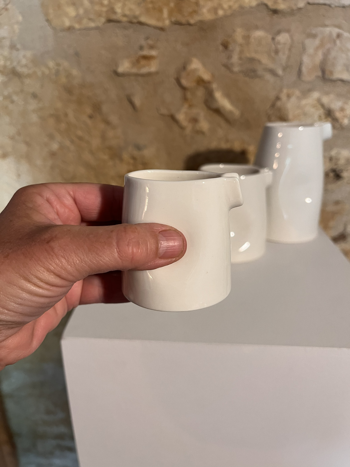 Main tenant une saucière verseuse en porcelaine blanche devant les autres tailles, sur socle