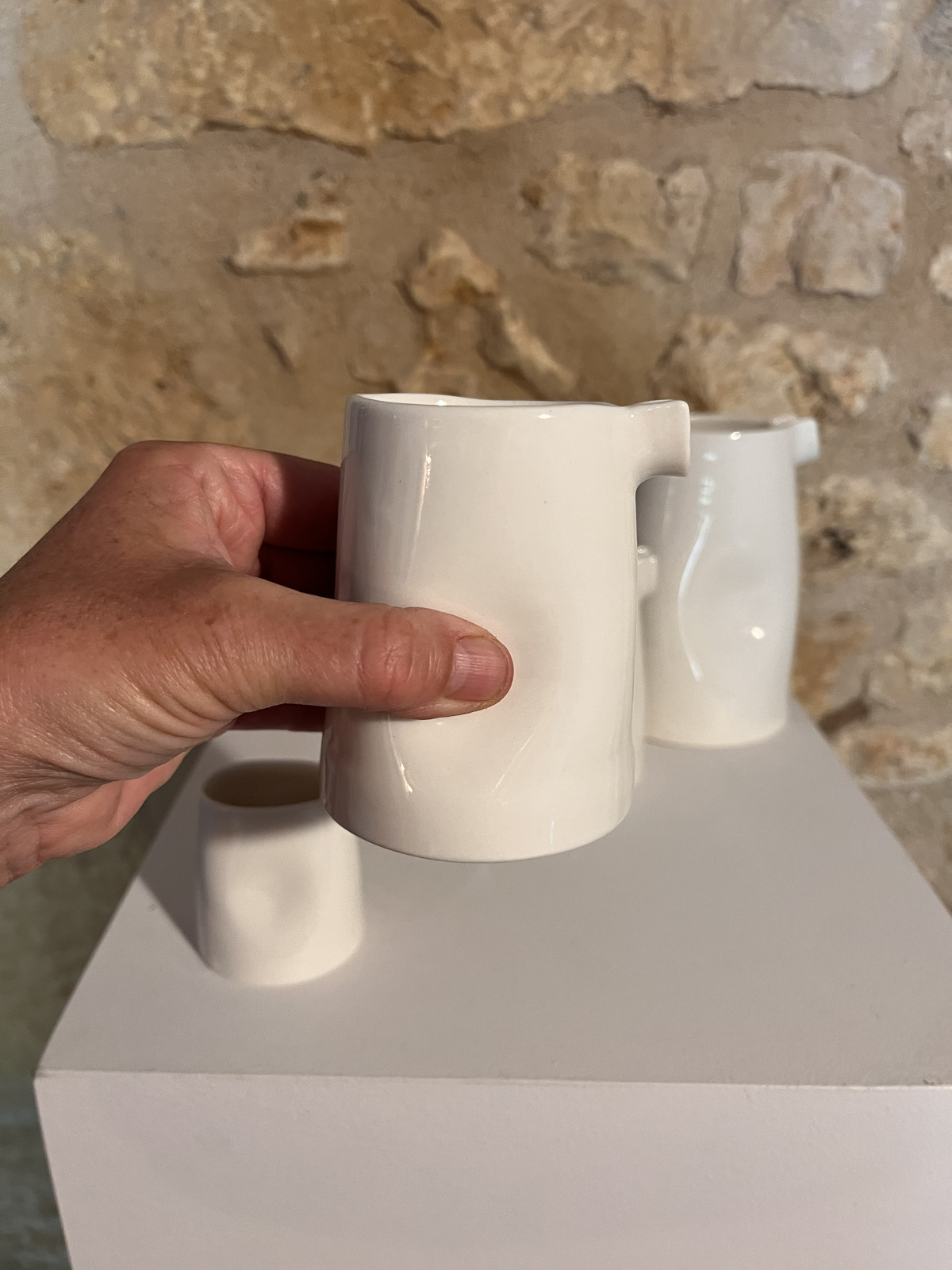 Main tenant le grand modèle de la saucière verseuse en porcelaine blanche, petits modèles derrière