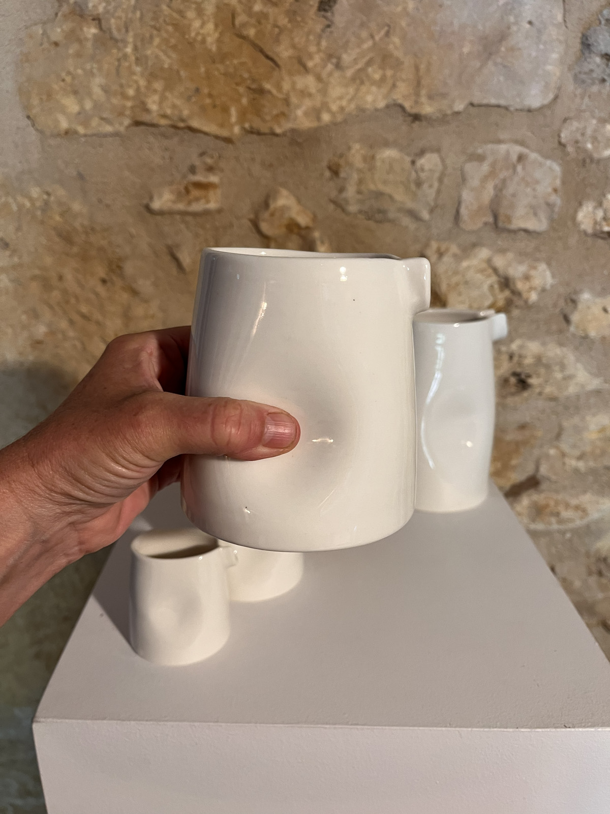 Main tenant la grande saucière verseuse en porcelaine blanche par son renfoncement, petites saucières derrière