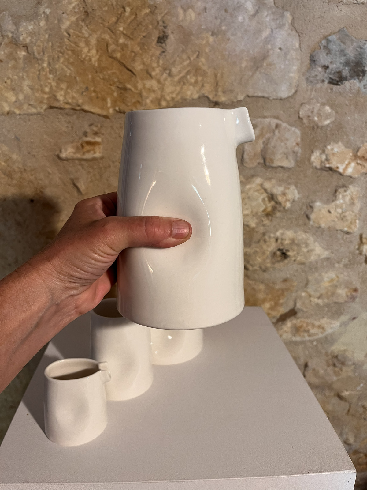 Main saisissant la grande saucière verseuse en porcelaine blanche par son renfoncement, sur socle