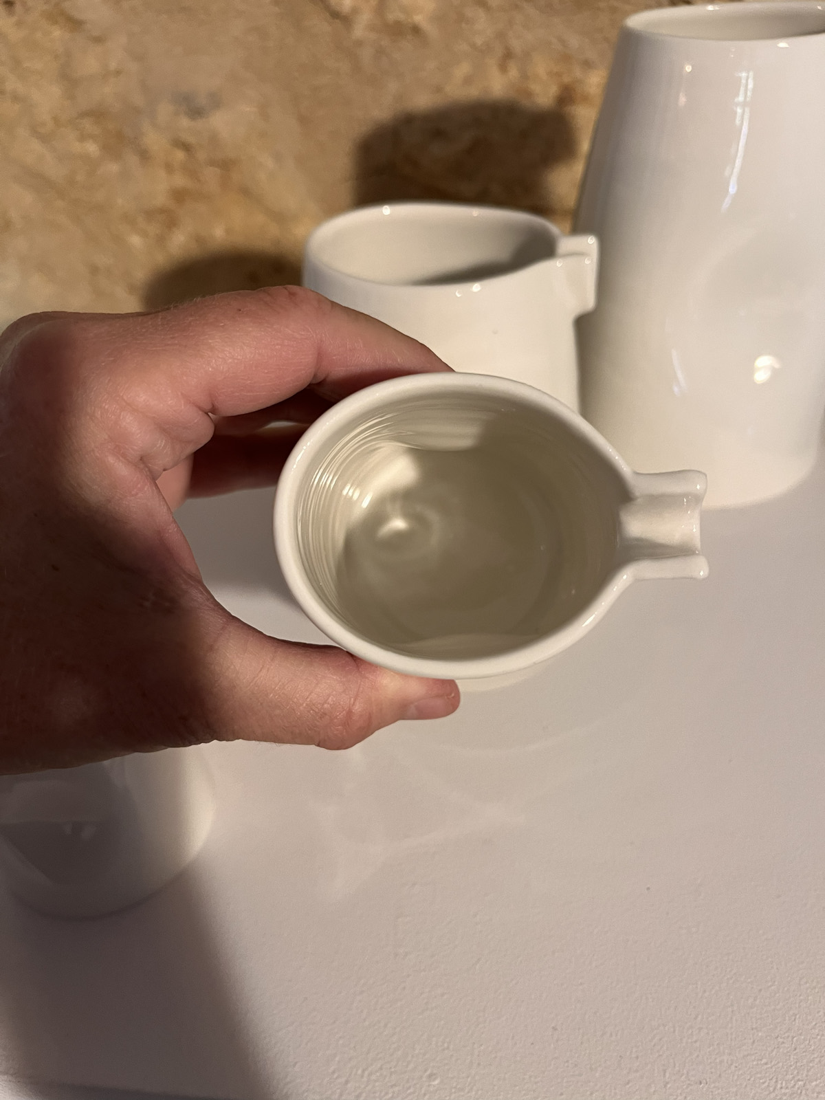 Saucière verseuse en porcelaine blanche tenue en main et vue de dessus, bec verseur et intérieur strié