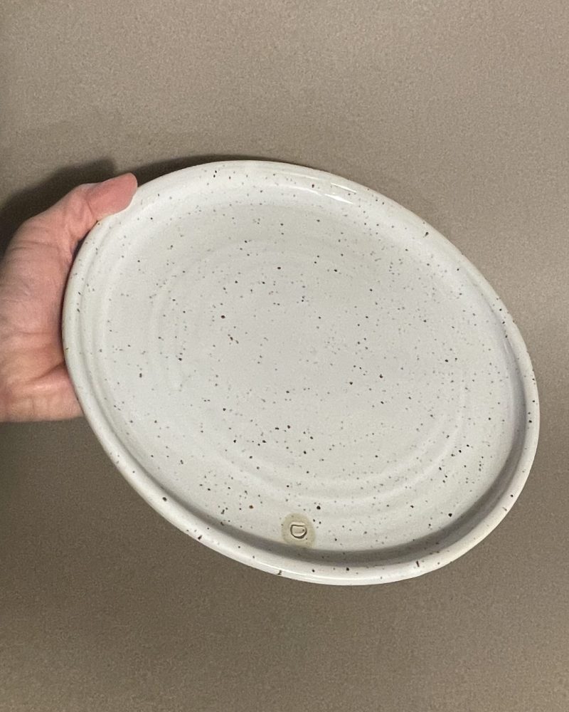 Assiette plate Maya en grès pyrité émaillé blanc brillant tenue en main, logo adb en creux