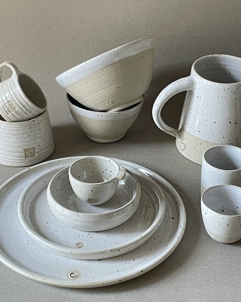 Ensemble de la collection Maya vu de trois quarts : assiettes empilées, bols, tasses, gobelets et pichet