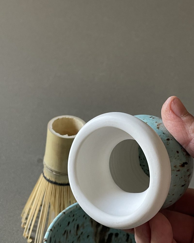 Repose-fouet à matcha Osaka en porcelaine tenu en main, intérieur blanc et extérieur céladon, fouet en bambou