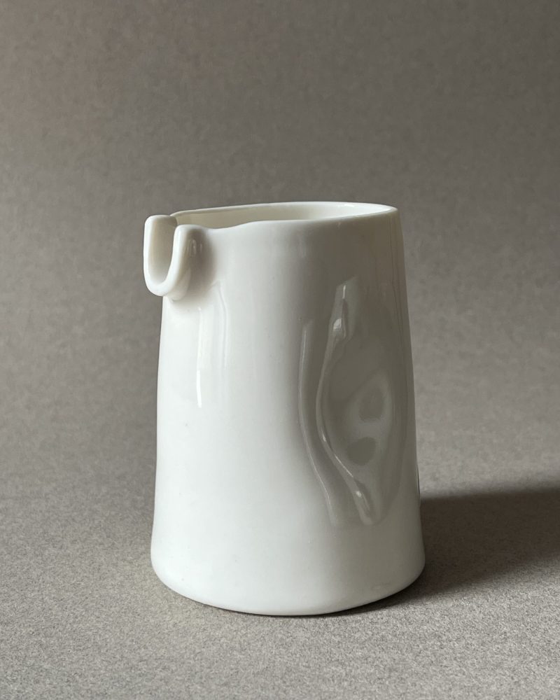 Petite saucière verseuse en porcelaine blanche brillante à renfoncements, vue de face sur fond gris