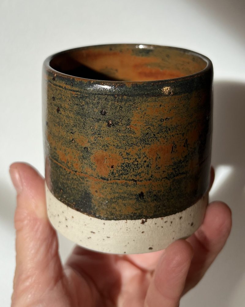 Gobelet Steph en grès à l'émail automne brillant, orange et vert sombre, tenu en main, base brute