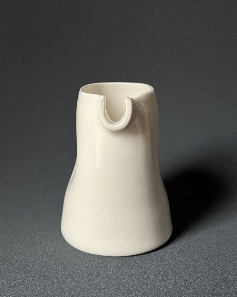Saucière verseuse en porcelaine blanche vue de face, bec verseur en U et parois pincées, fond sombre