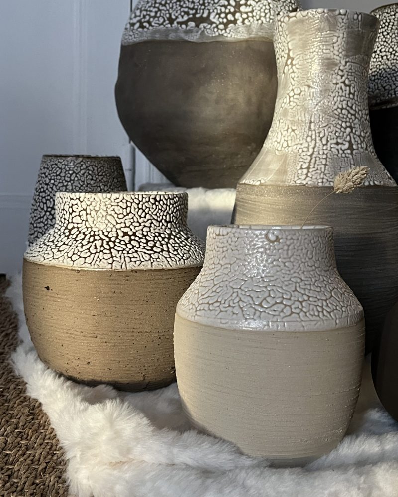 Vases Winter en grès beige et brun aux cols émaillés blanc rétracté, posés sur une peau blanche, vue rapprochée