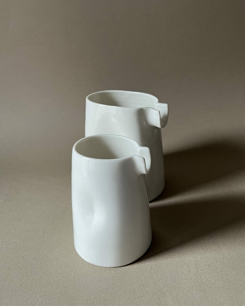 Deux saucières verseuses en porcelaine blanche de tailles différentes, becs en U, sur fond beige