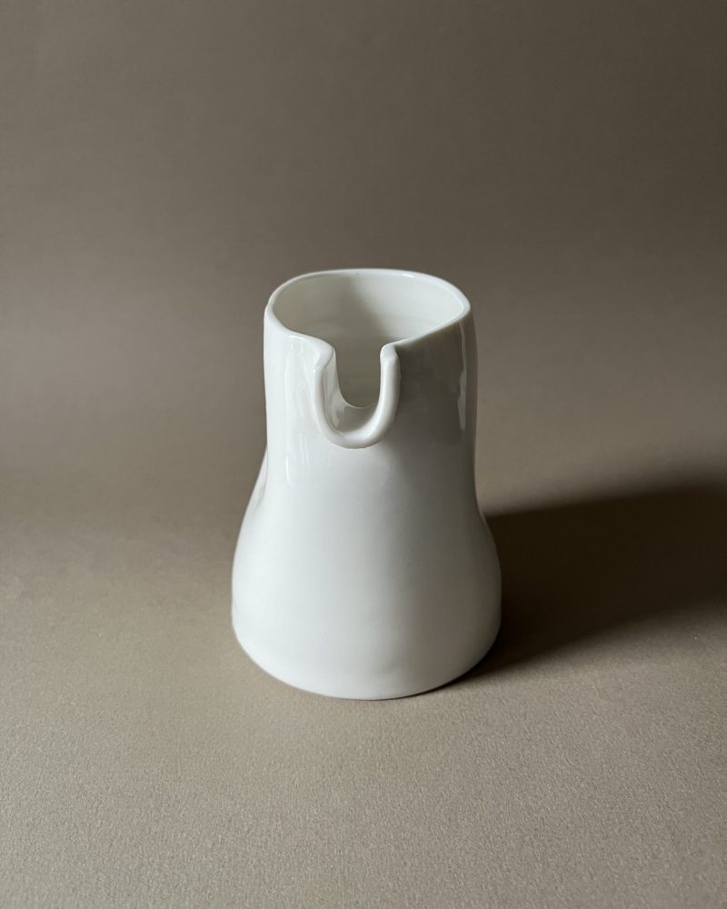 Petite saucière verseuse en porcelaine blanche vue de face, bec en U, sur fond beige