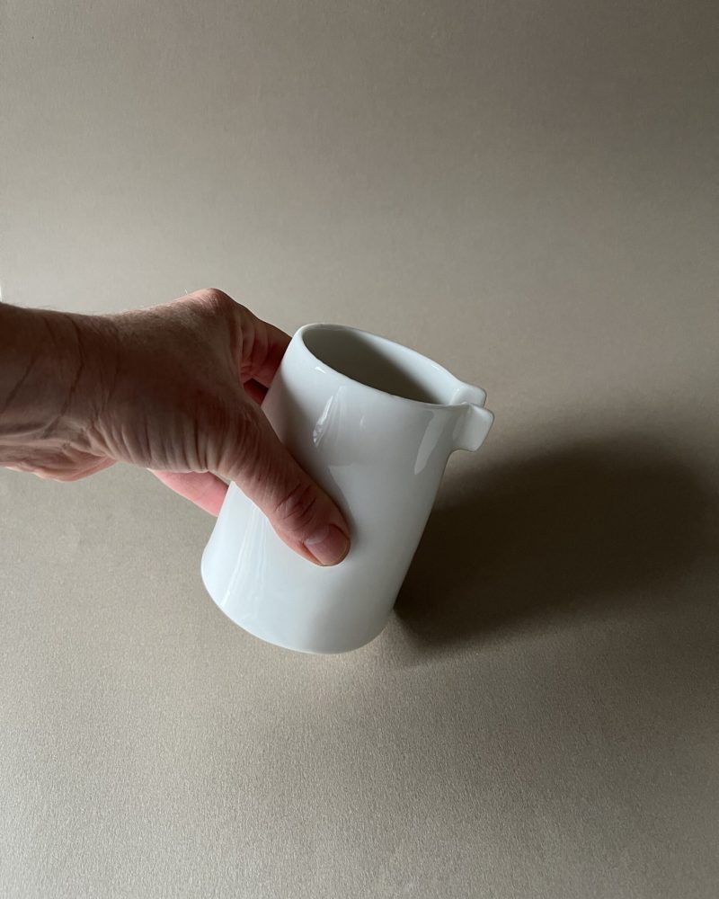 Petite saucière verseuse en porcelaine blanche tenue en main par son renfoncement