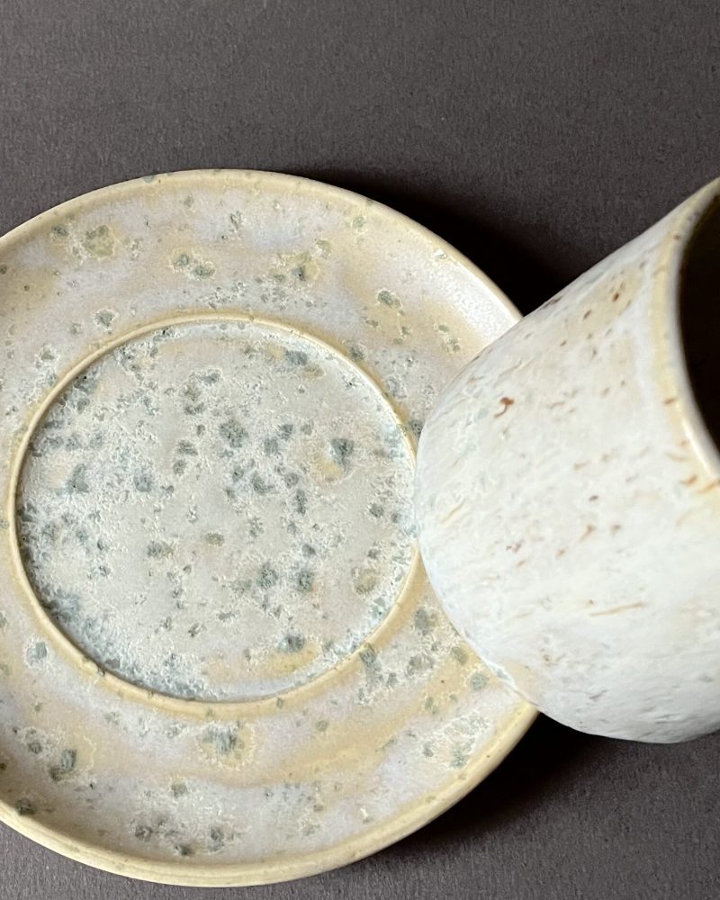 Gros plan sur la soucoupe Steph à l'émail satiné tacheté de vert, tasse posée sur le bord