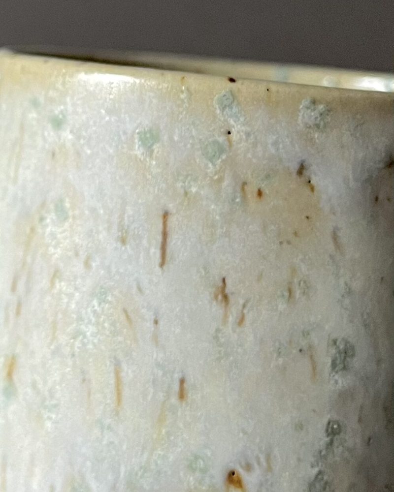 Gros plan sur la paroi de la tasse Steph, émail satiné blanc, beige et vert avec taches brillantes