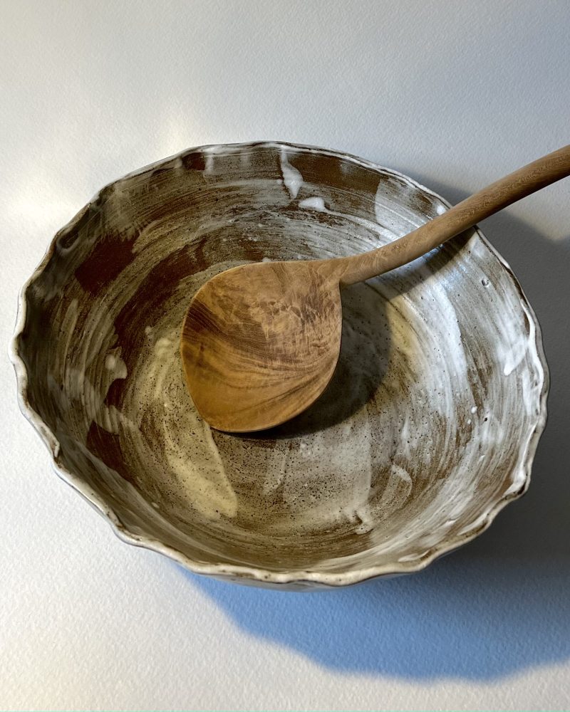 Saladier marbré marron et blanc vu de dessus avec une grande cuillère en bois posée dedans