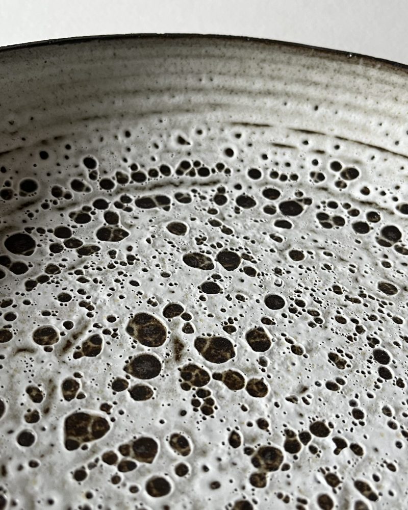 Gros plan sur l'émail blanc velours à pastilles découvertes de grès noir d'une coupe Rocaille