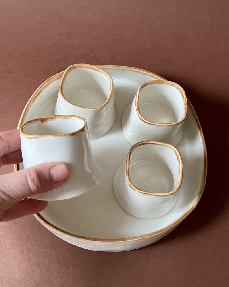Tasse Ulysse à liseré marron tenue en main au-dessus du plateau et des trois autres tasses