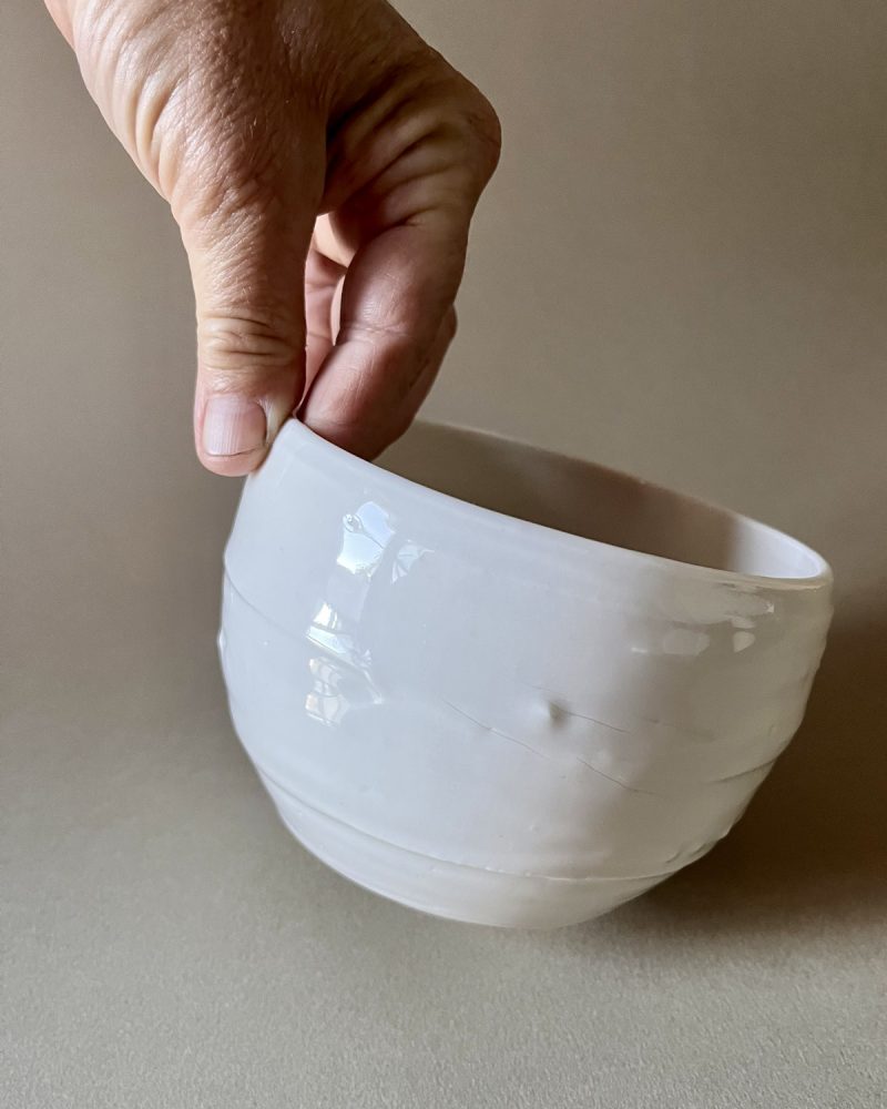 Bol Purete en porcelaine blanche tenu par le bord entre deux doigts, émail brillant